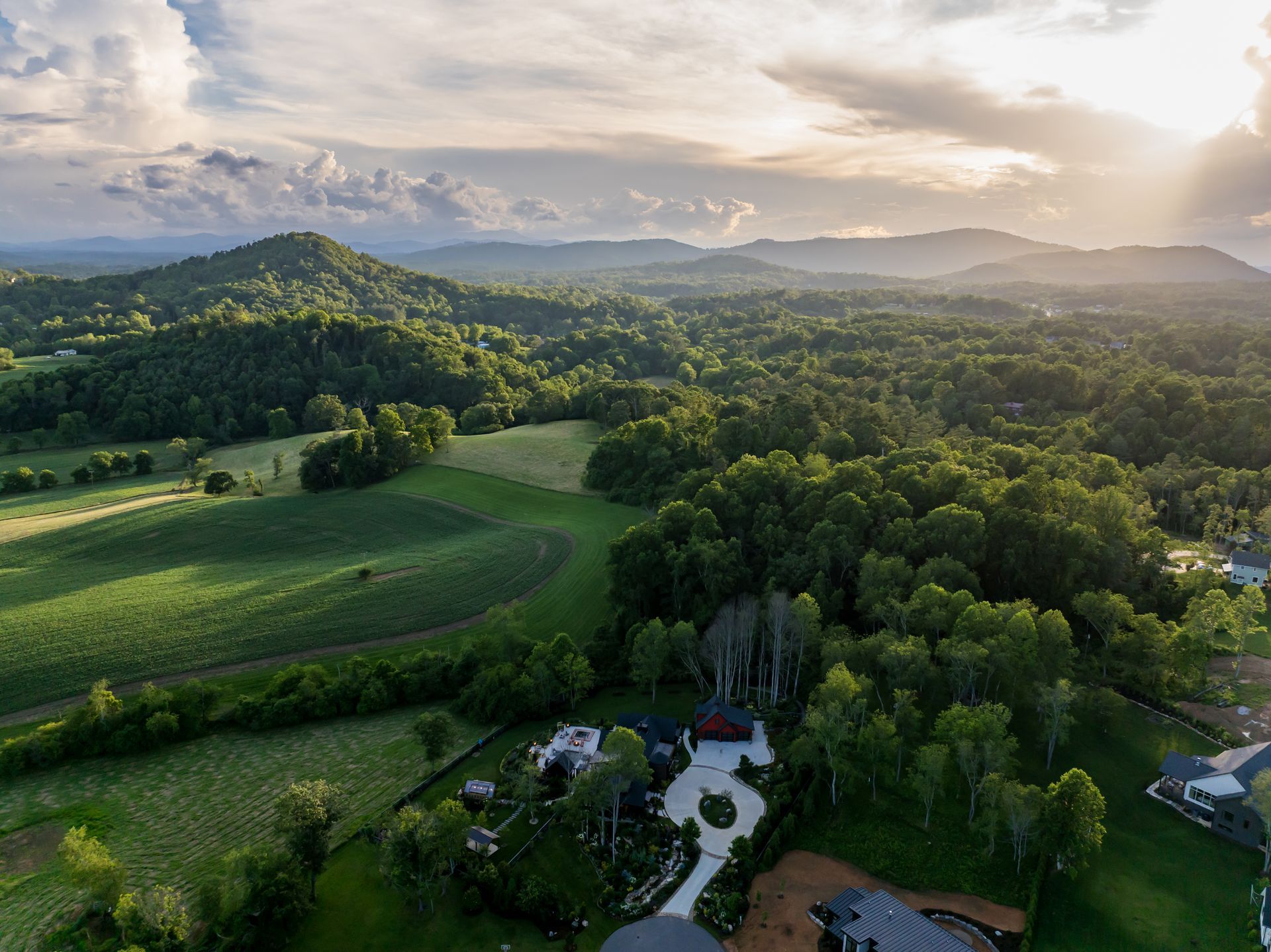 Sunlit green hills and forest with a winding path under a cloudy sky