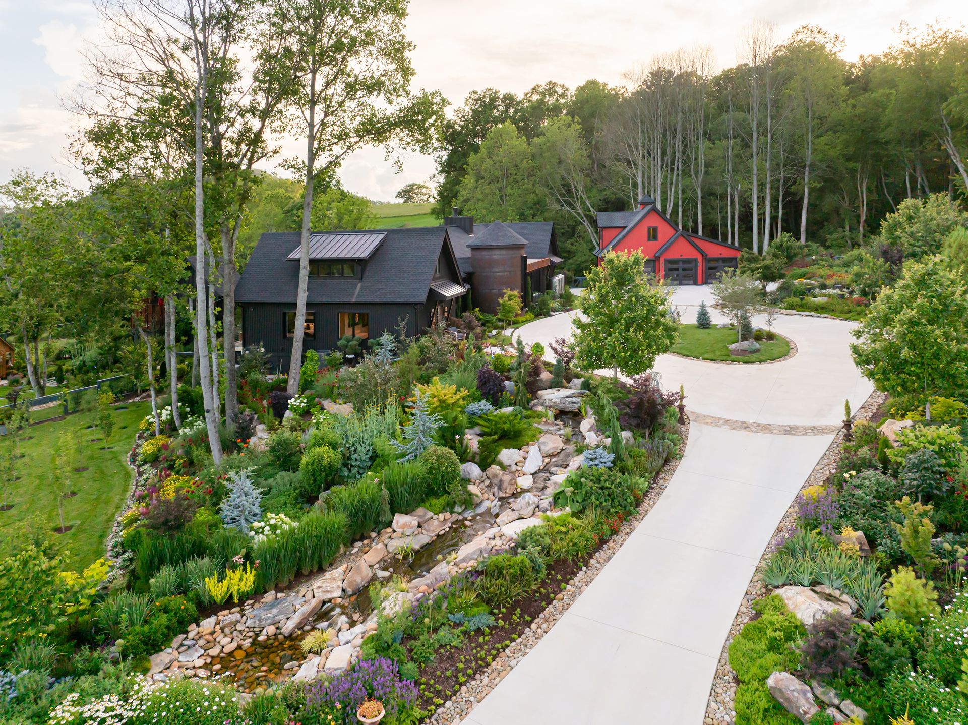 Winding garden path past black and red houses surrounded by lush greenery and trees