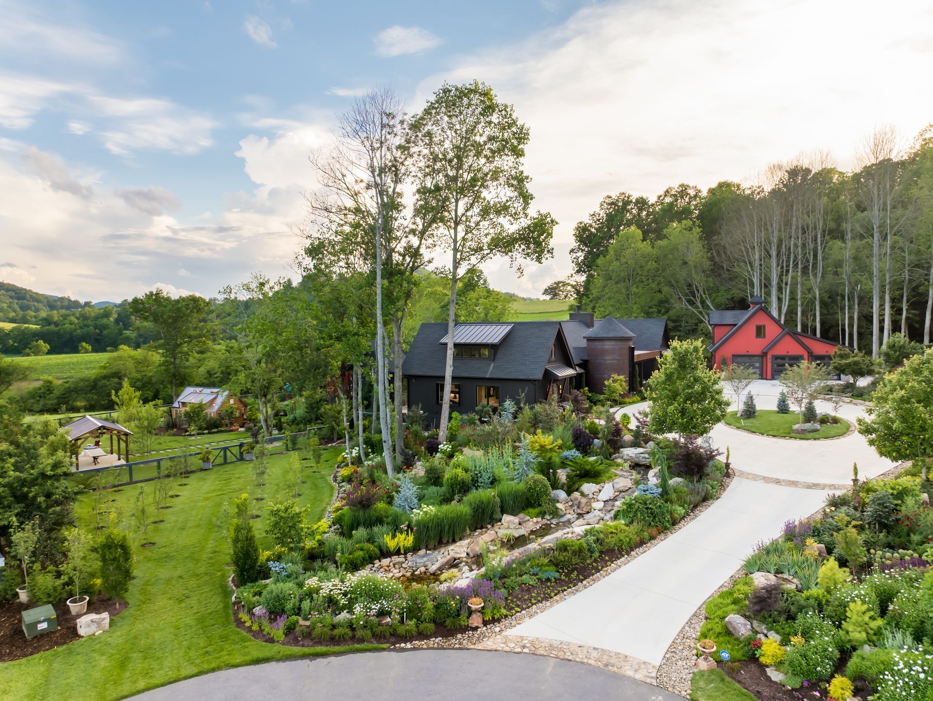 Landscaped country garden with winding path, flowers, trees, and two houses under a cloudy sky