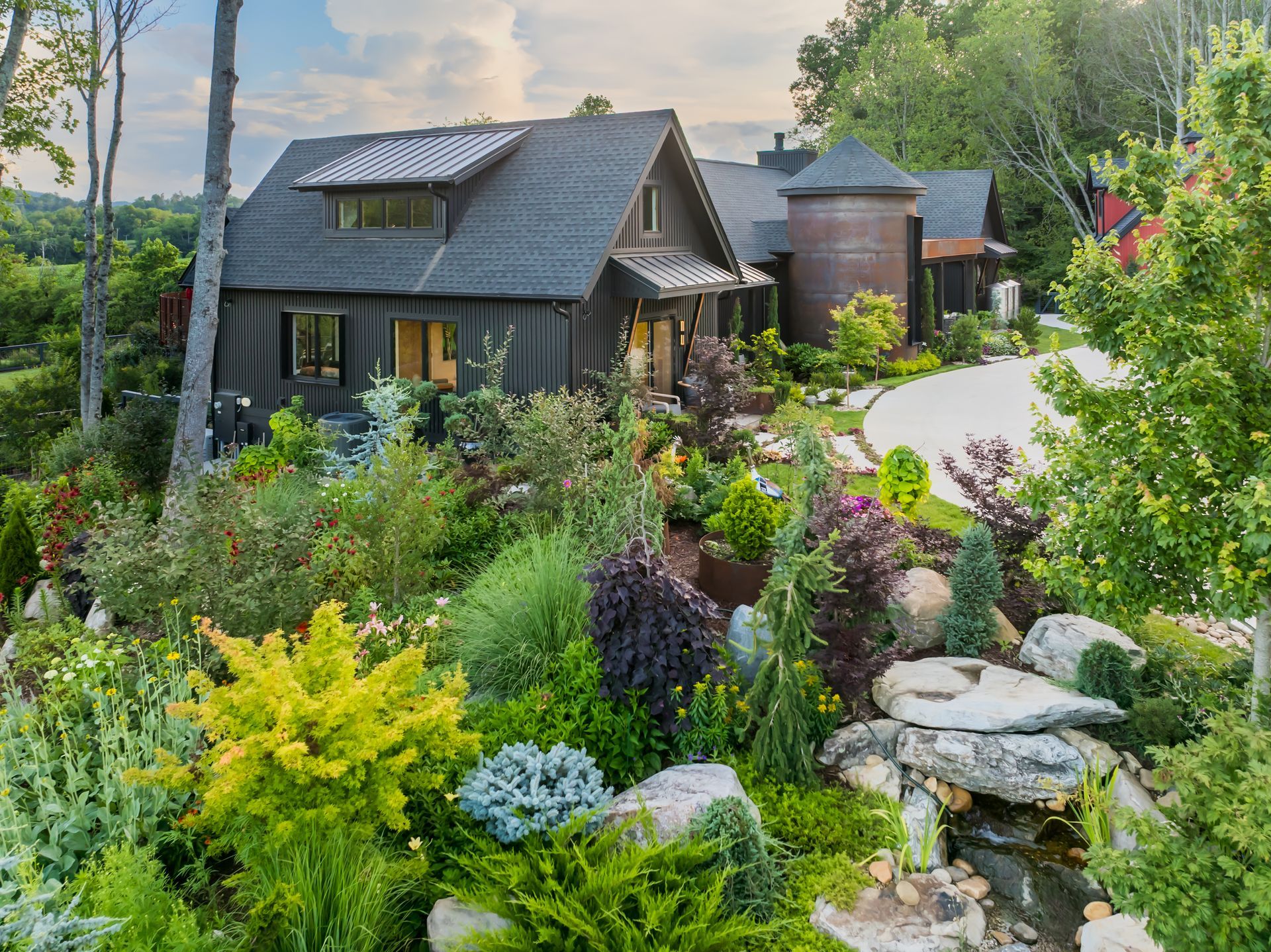 Lush garden path leading to a dark cabin beside a water tank at sunset