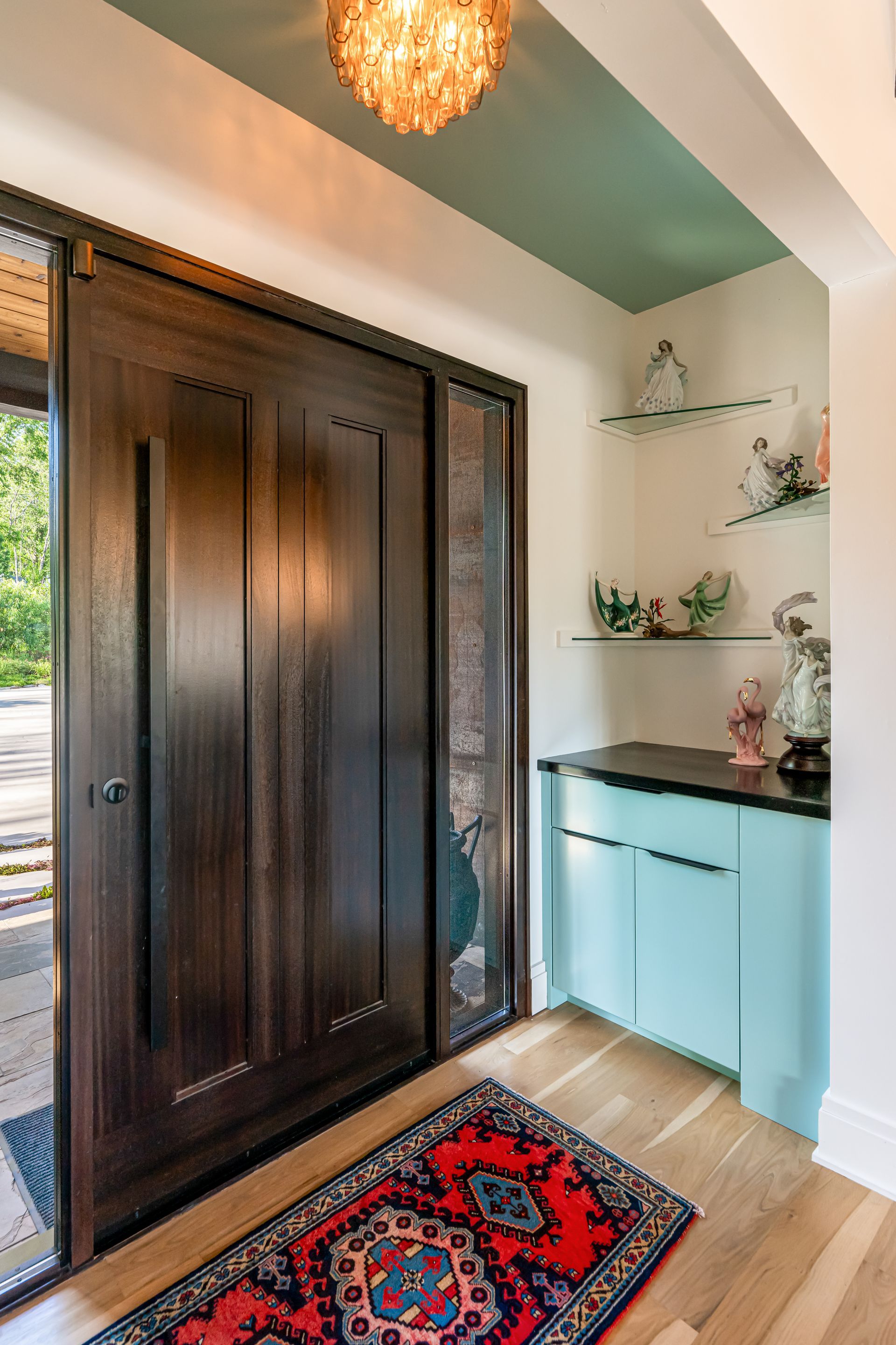 Entryway with dark wood door, mint bench, shelf decor, and patterned rug under a pendant light.