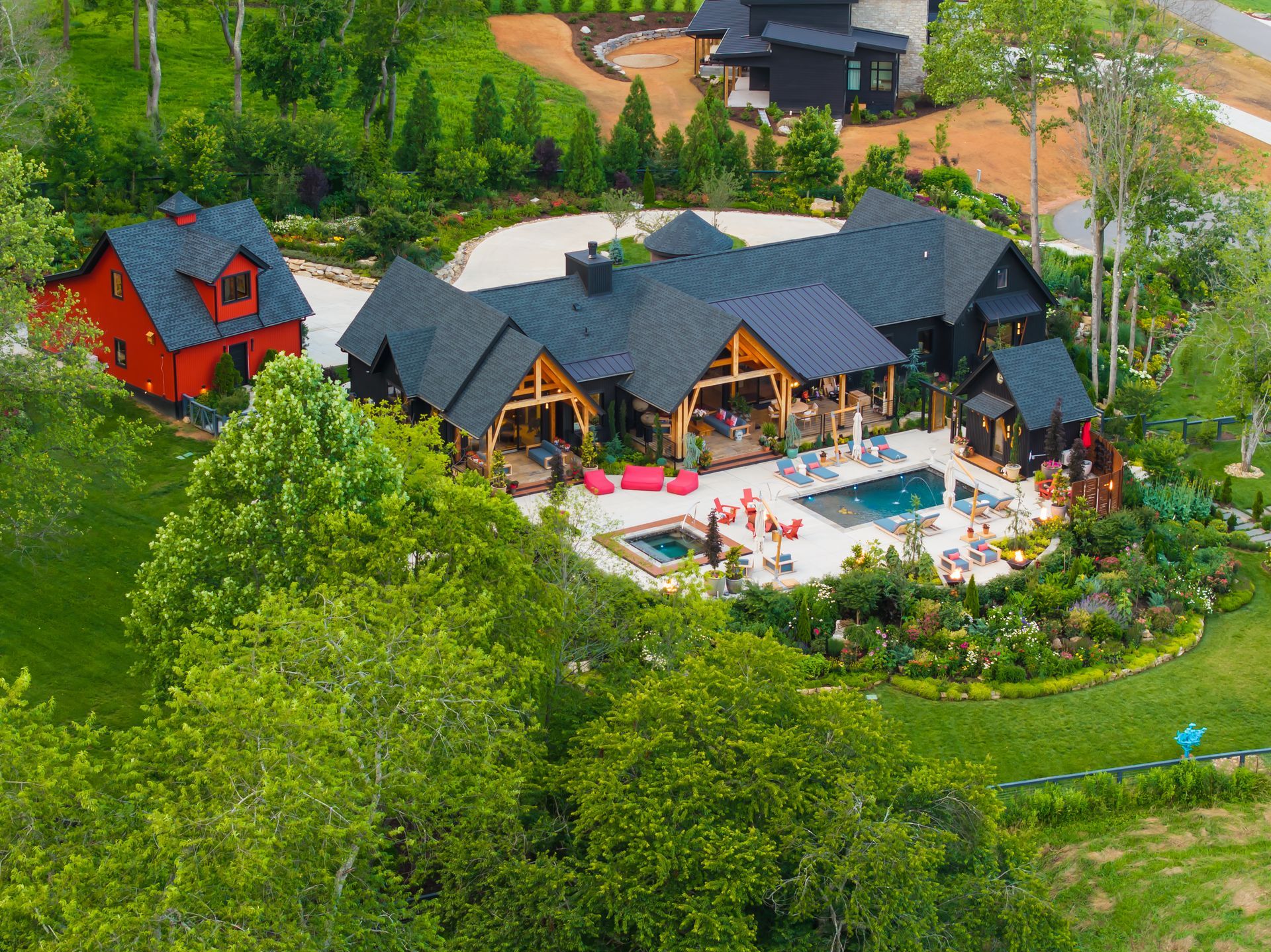 Aerial view of a lakeside resort with dark-roofed cabins, a pool, and lush green trees