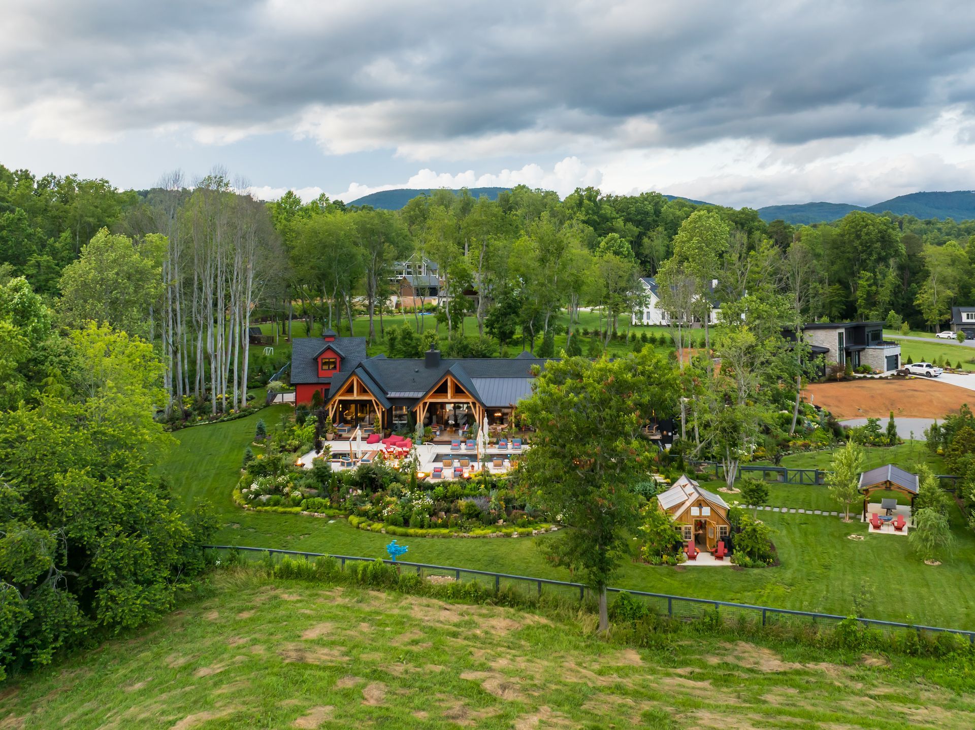Aerial view of a countryside lodge with green trees, gardens, and a cloudy sky