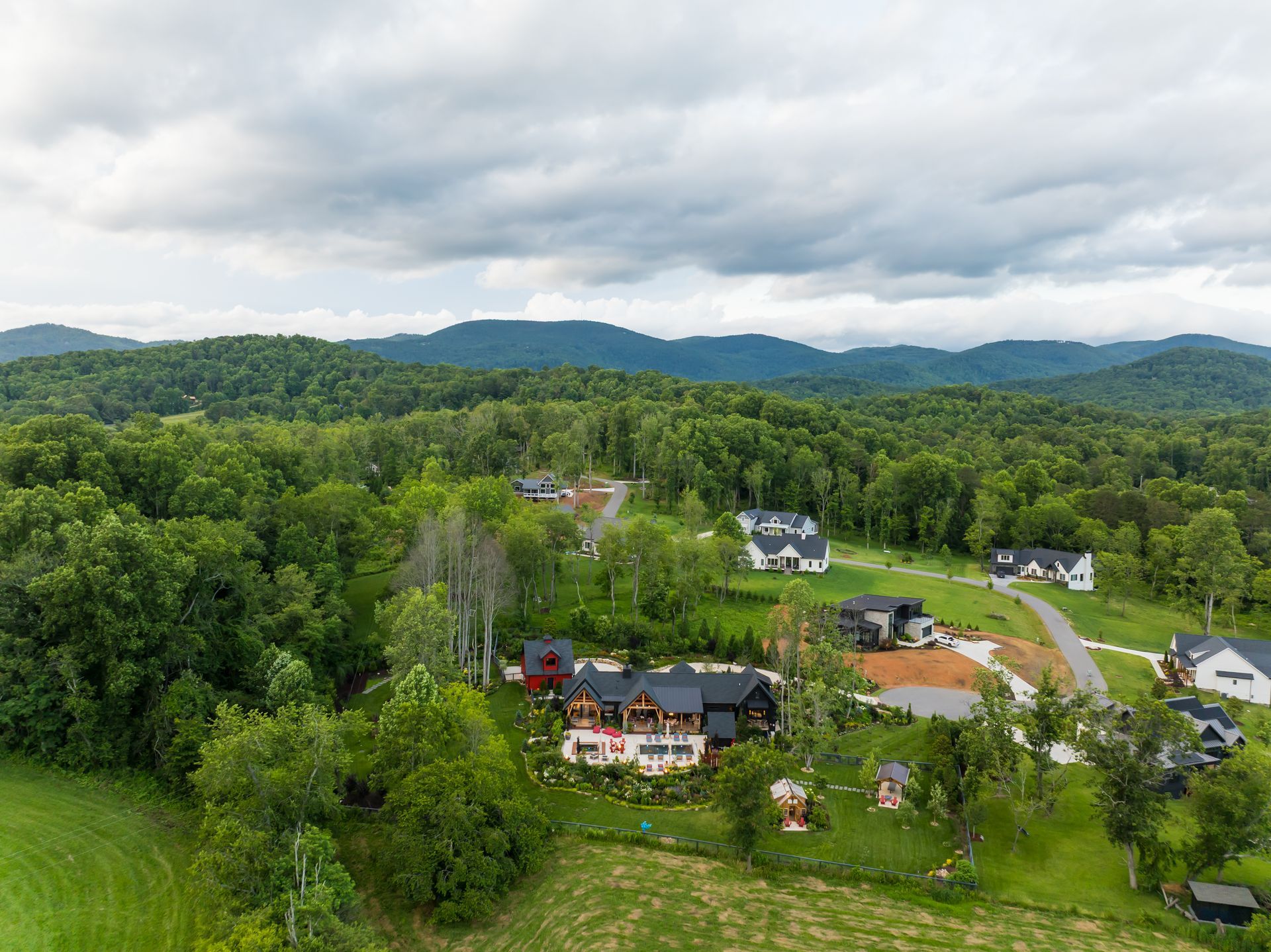 Aerial view of a green rural neighborhood with houses, trees, and mountains under cloudy skies