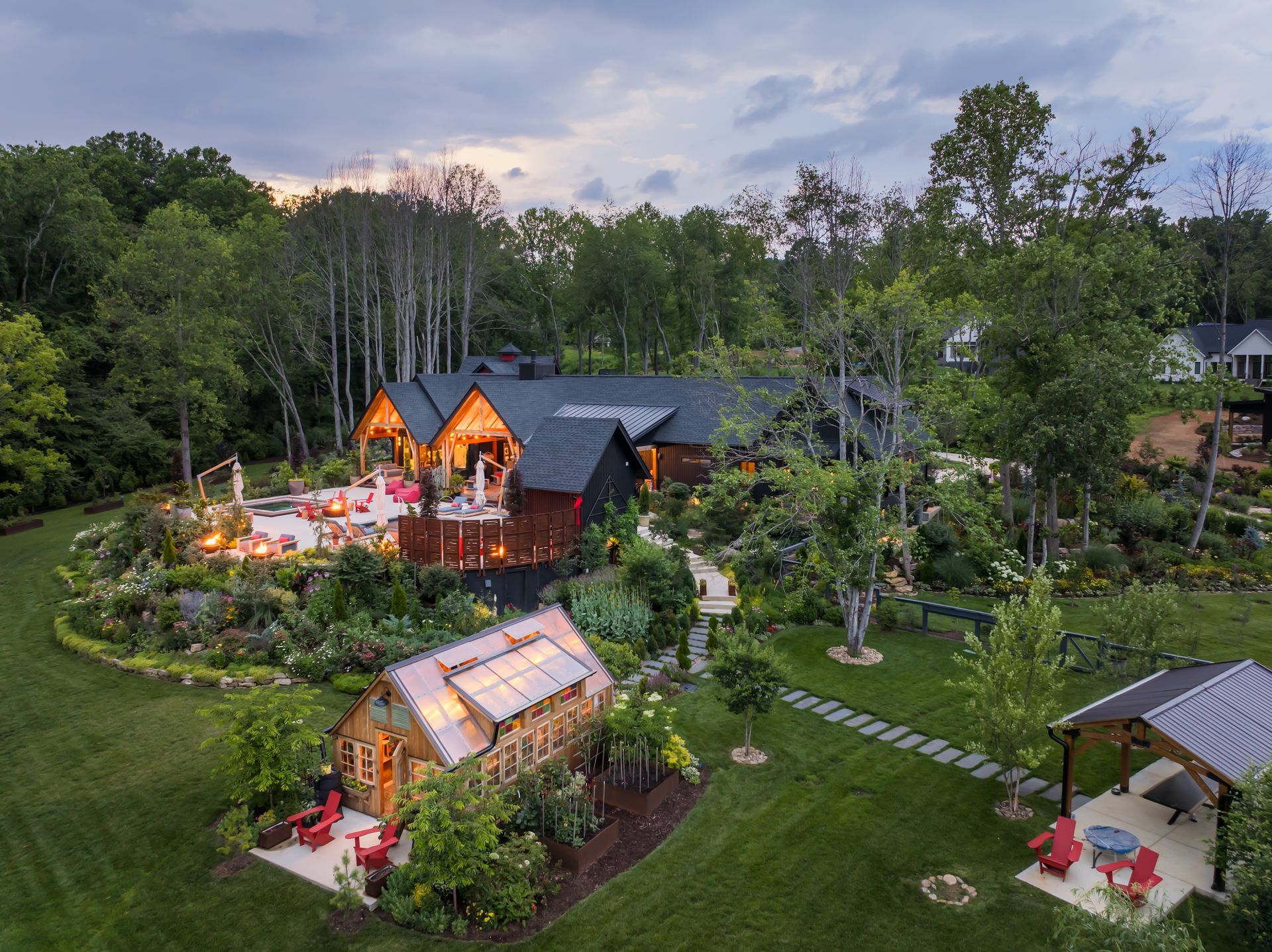 Lush garden resort with lit cabins, greenhouse, and pavilion at dusk, surrounded by trees