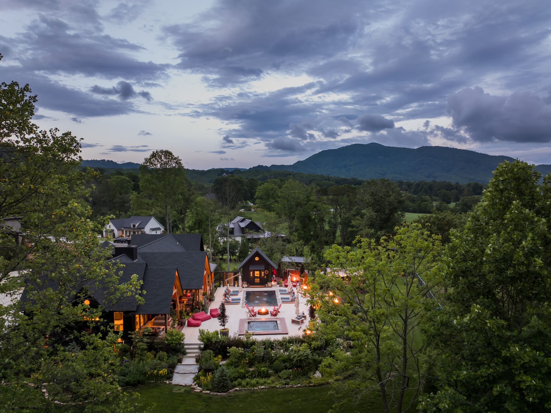 Lit temple courtyard among trees at dusk, with distant mountains under a cloudy sky.