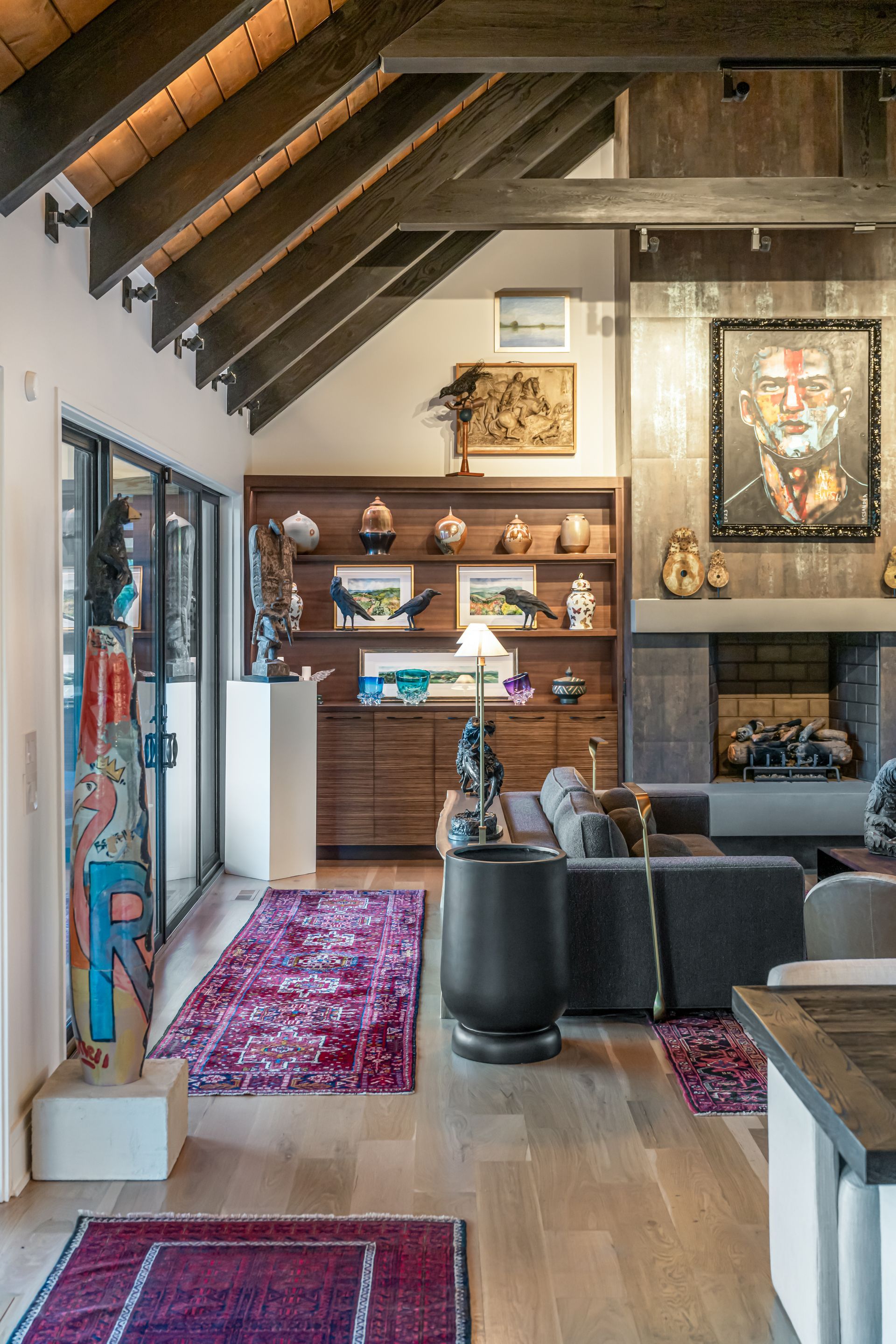Cozy loft living room with wood beams, bookshelves, dark sofa, fireplace, and colorful rug