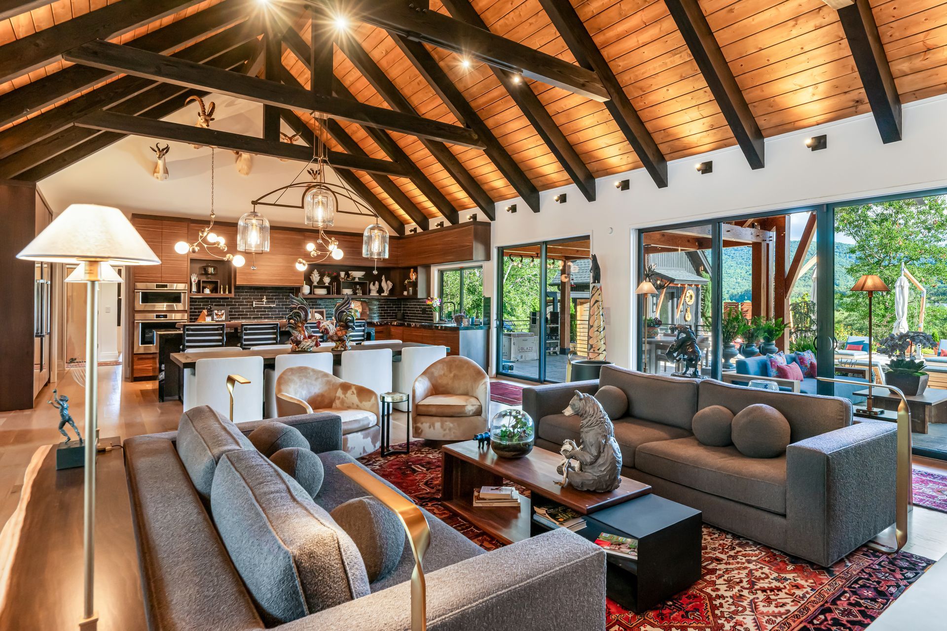 Spacious modern living room with vaulted wood ceiling, sofas, red rug, and open view to a patio and greenery