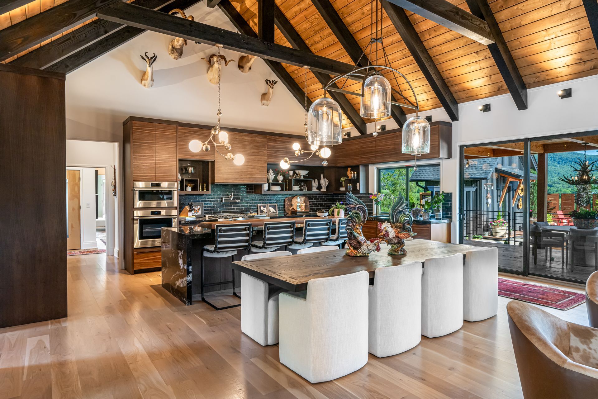 Modern open-concept kitchen and dining area with wood beams, island seating, and large windows overlooking a patio