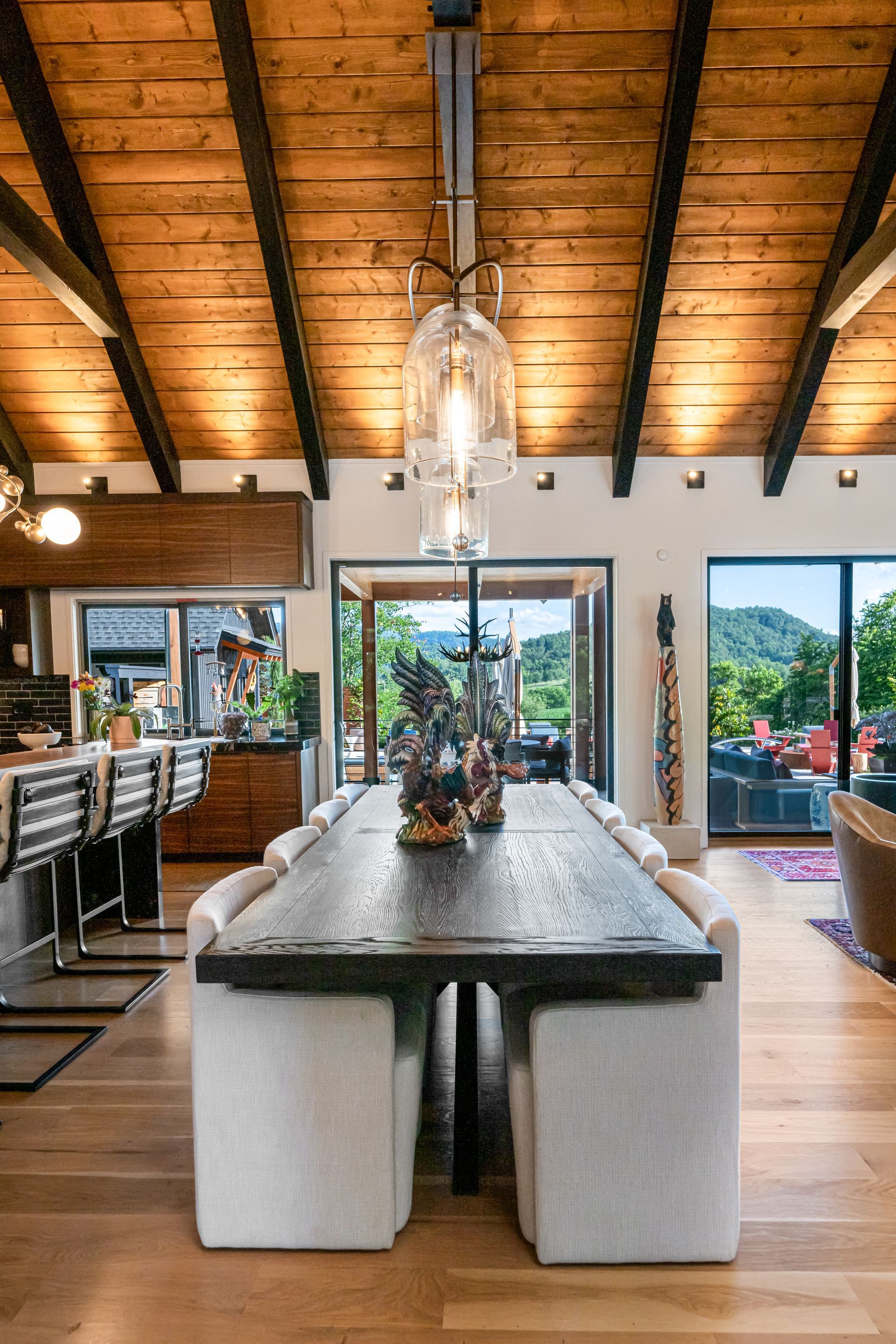 Open-air dining room with a long table, high vaulted wood ceiling, and garden view through sliding doors