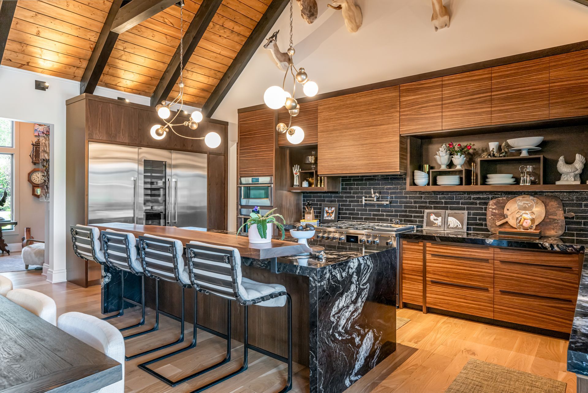 Modern kitchen with brick walls, vaulted wood ceiling, black island stools, and stainless appliances