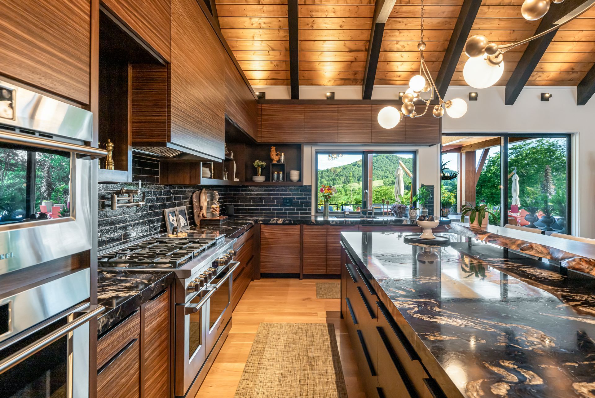 Modern kitchen with wood ceiling, dark cabinets, stainless appliances, and a large stone island with stools