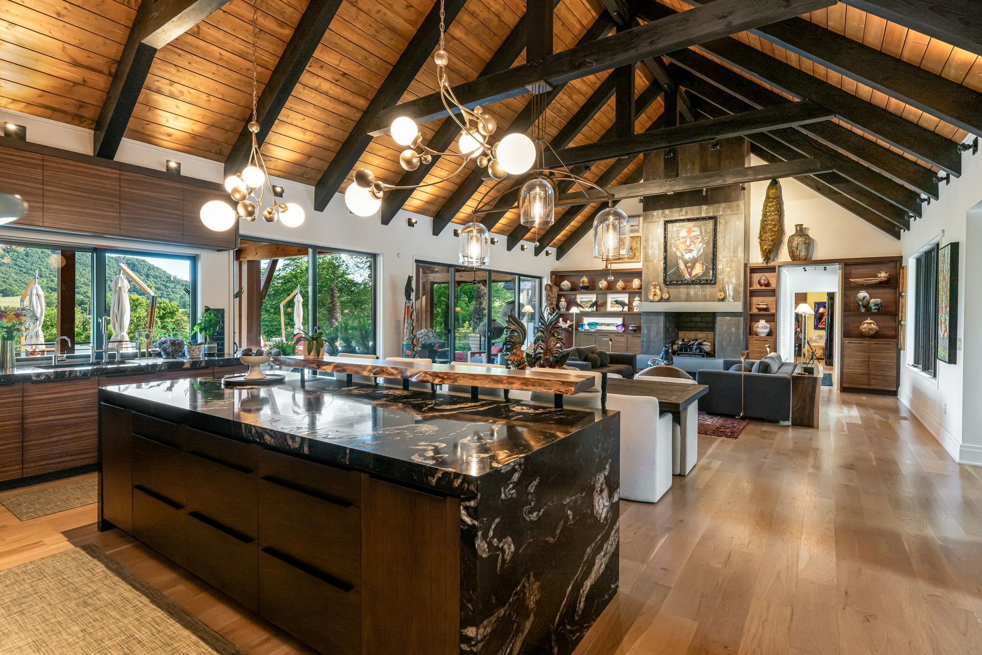 Spacious modern kitchen with dark island, wood beams, hanging lights, and large windows.