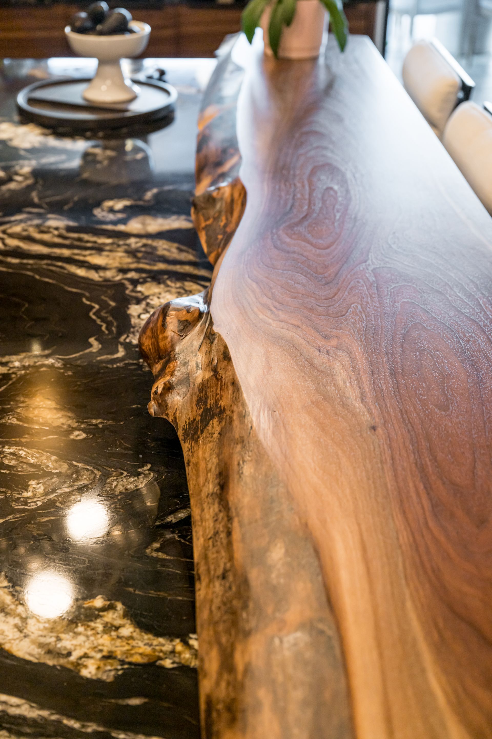 Close-up of a polished live-edge wood and black stone dining table with a glossy finish