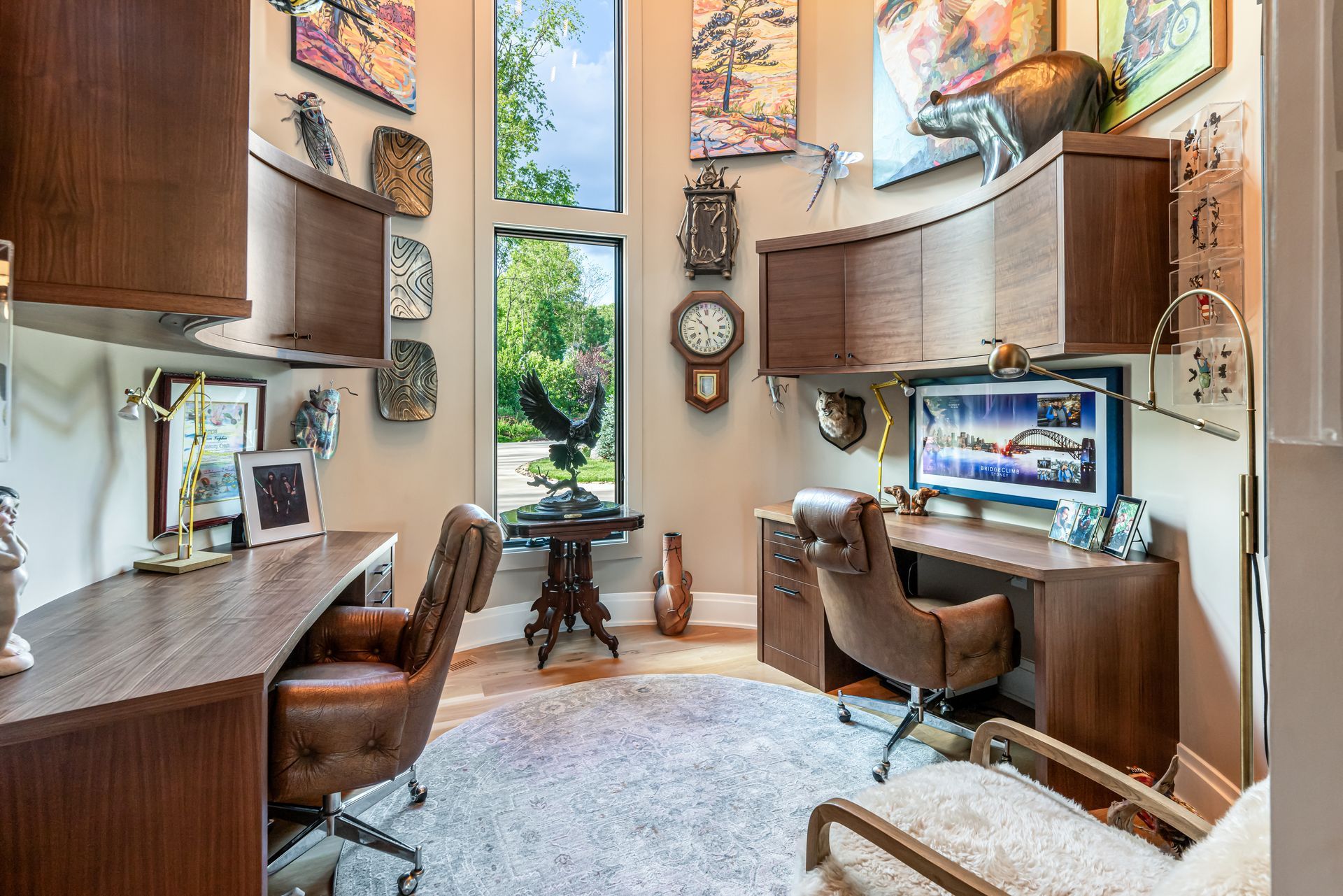 Modern home office with dual wooden desks, computers, and a tall window overlooking greenery