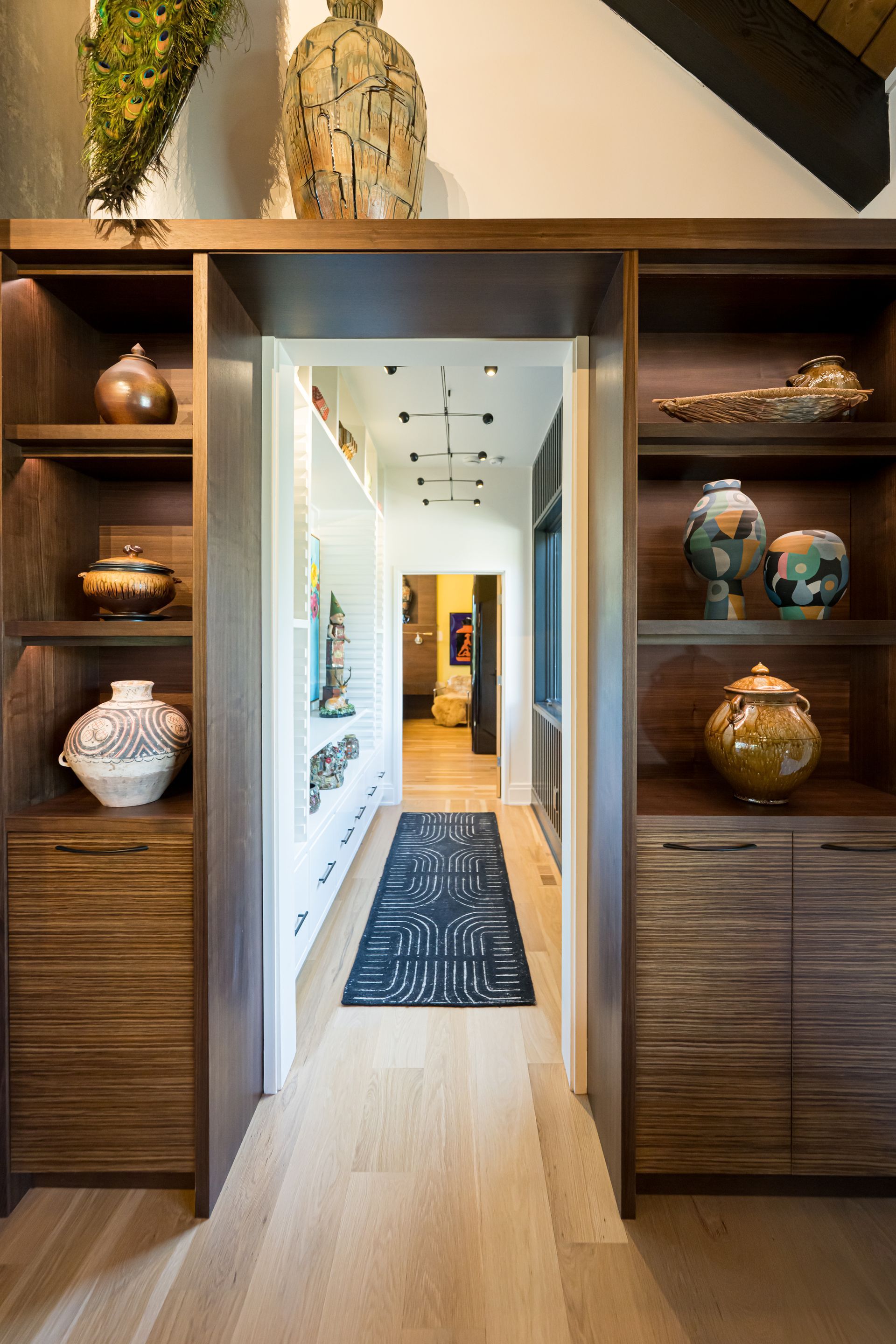 Open hallway with wood floors, built-in shelves, and decorative vases leading to a bright interior room
