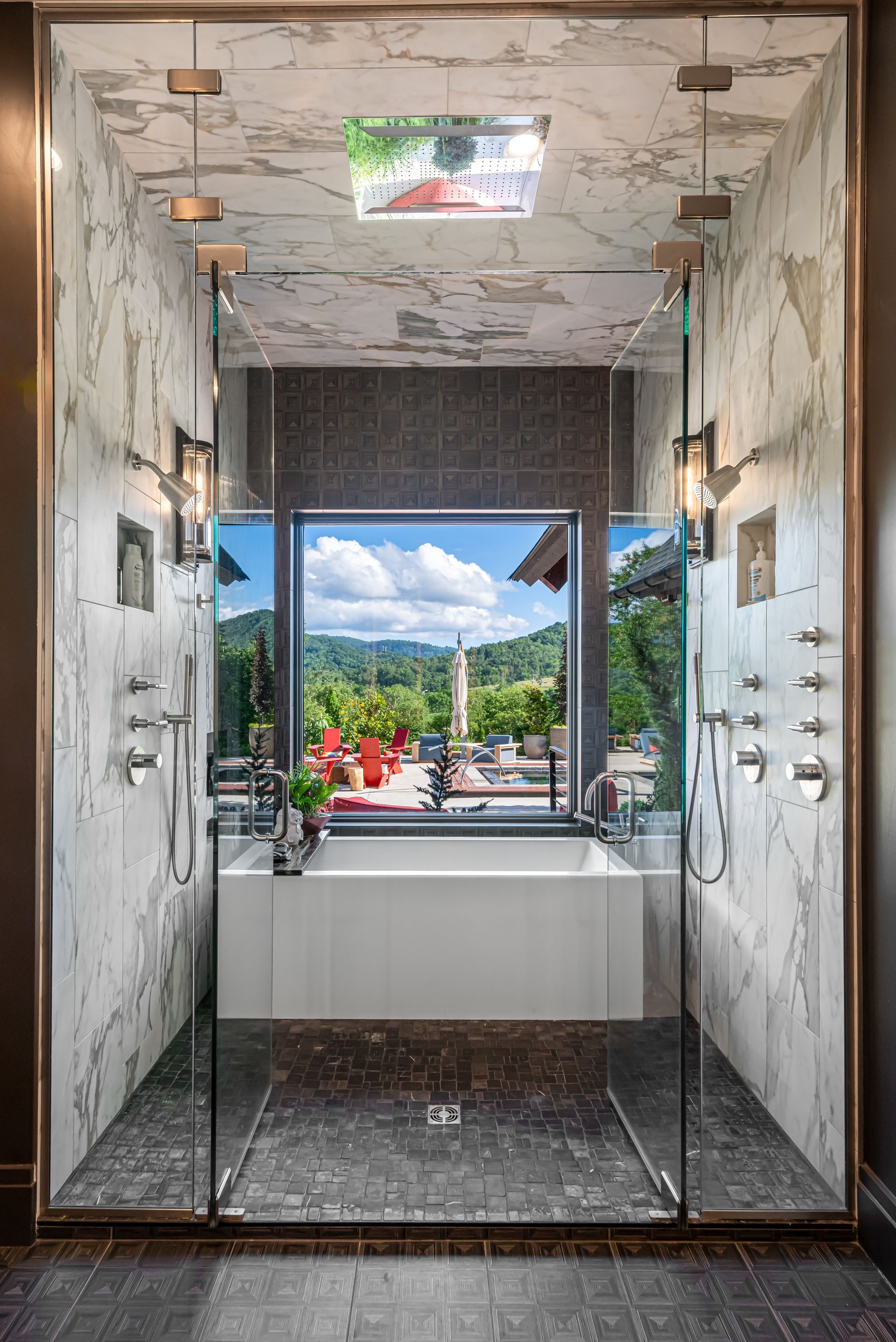 Mirrored shower stalls framing a bright outdoor pool and sky view through the open doorway