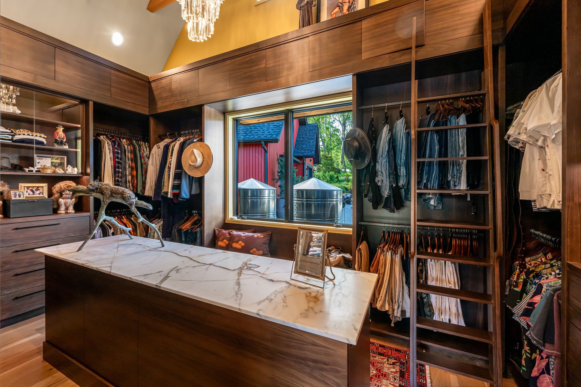 Walk-in closet with wooden shelving, hanging clothes, and a central island beneath a window.