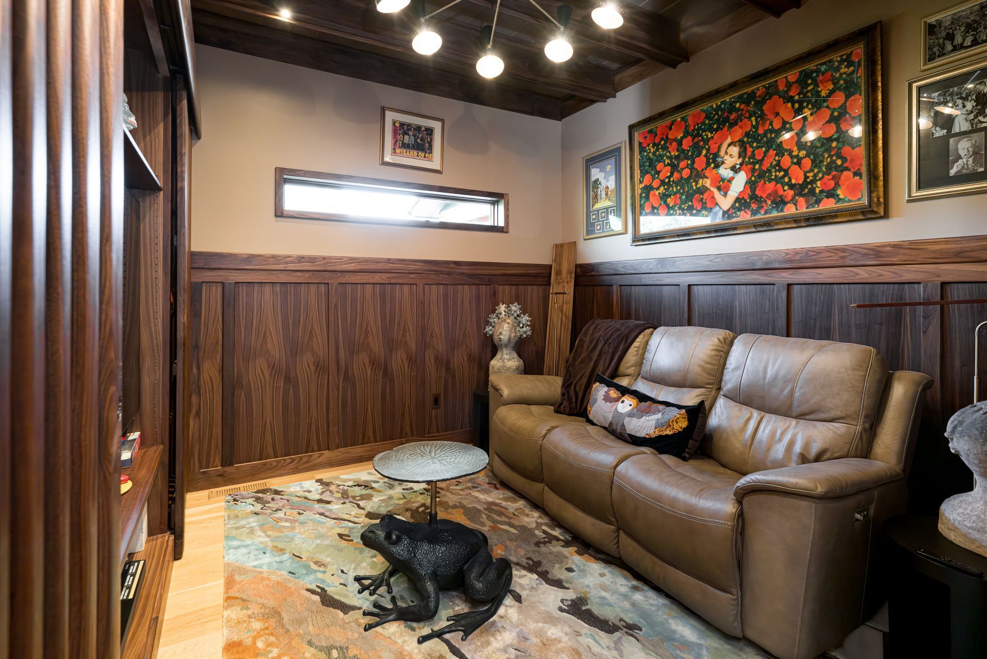 Cozy wood-paneled room with a leather sofa, dog bed, and black dog on a patterned rug under warm lights