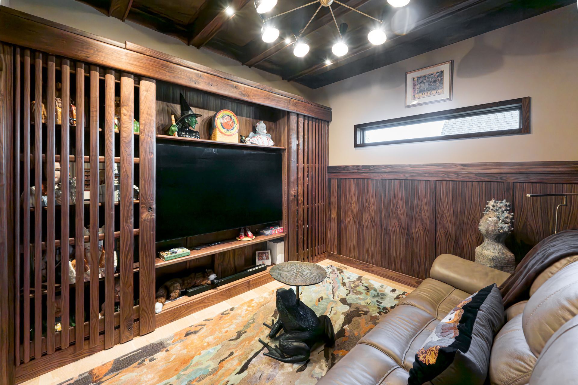 Cozy living room with wood-paneled walls, a large TV, leather sectional, and warm ceiling lights.