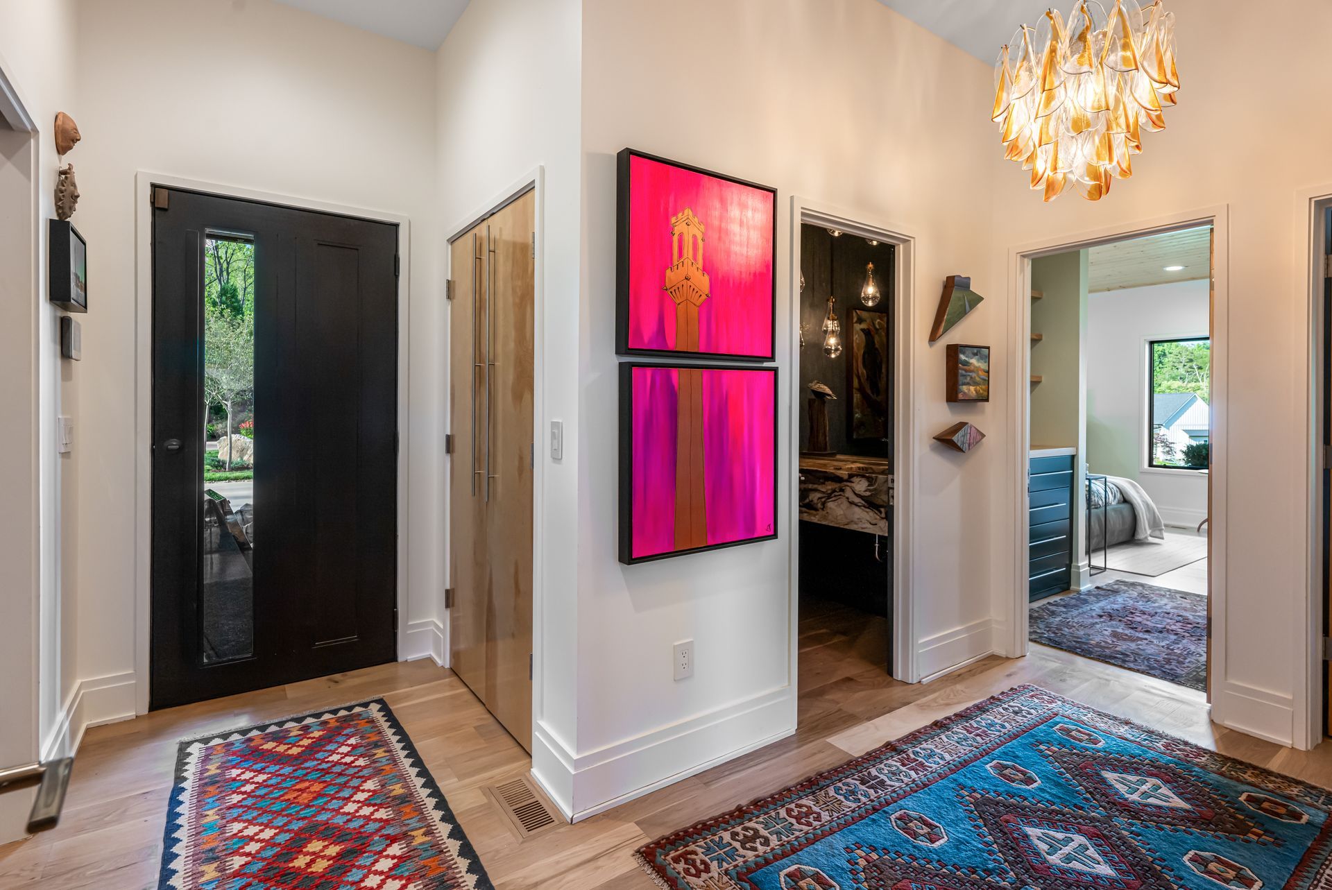Hallway with colorful wall art, patterned rugs, a chandelier, and doors to adjacent rooms.