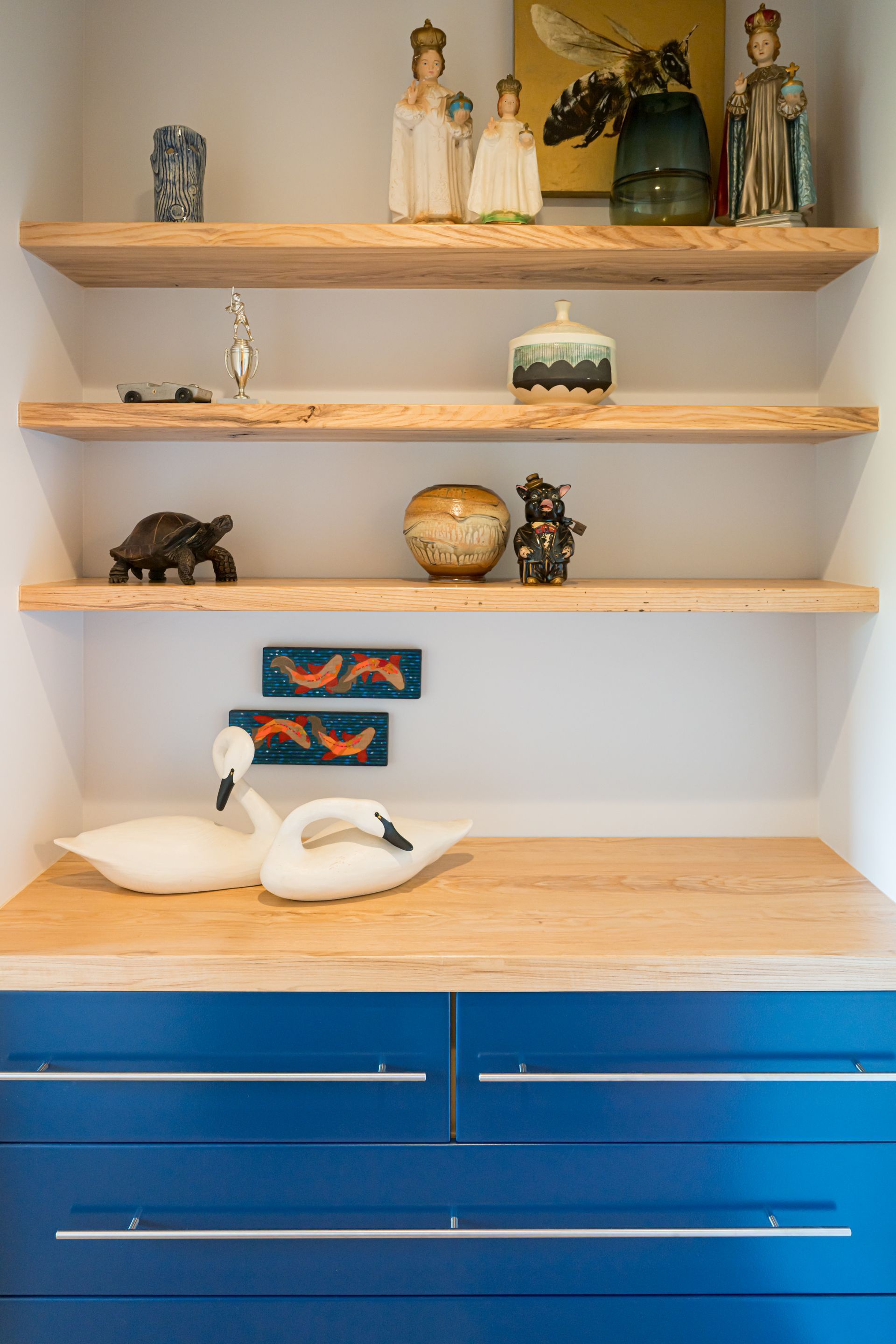 Built-in shelves with decorative figurines, bowls, and two white geese on a wooden countertop above blue drawers