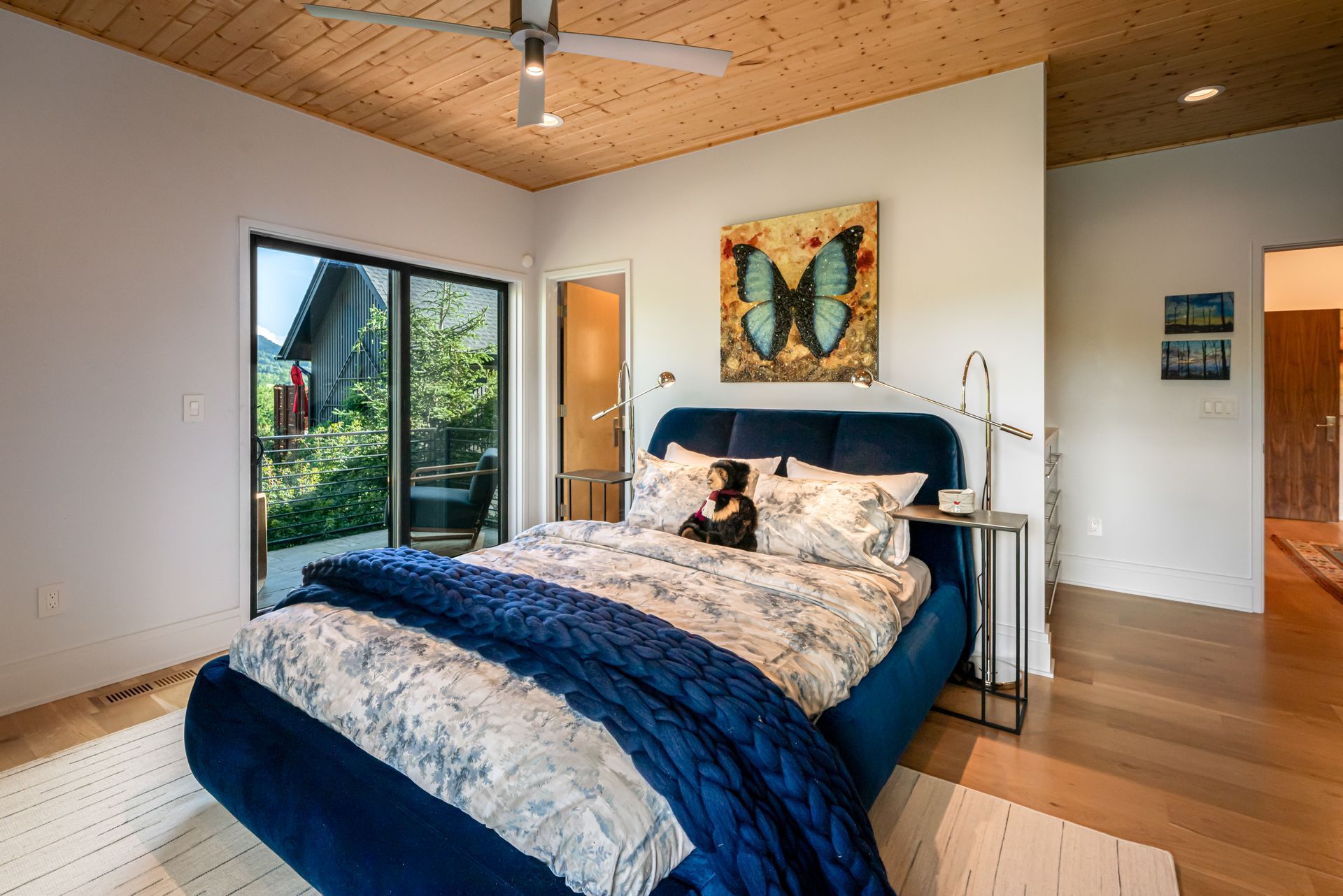 Modern bedroom with a blue bedspread, skylight, sliding glass doors, and warm wood floors