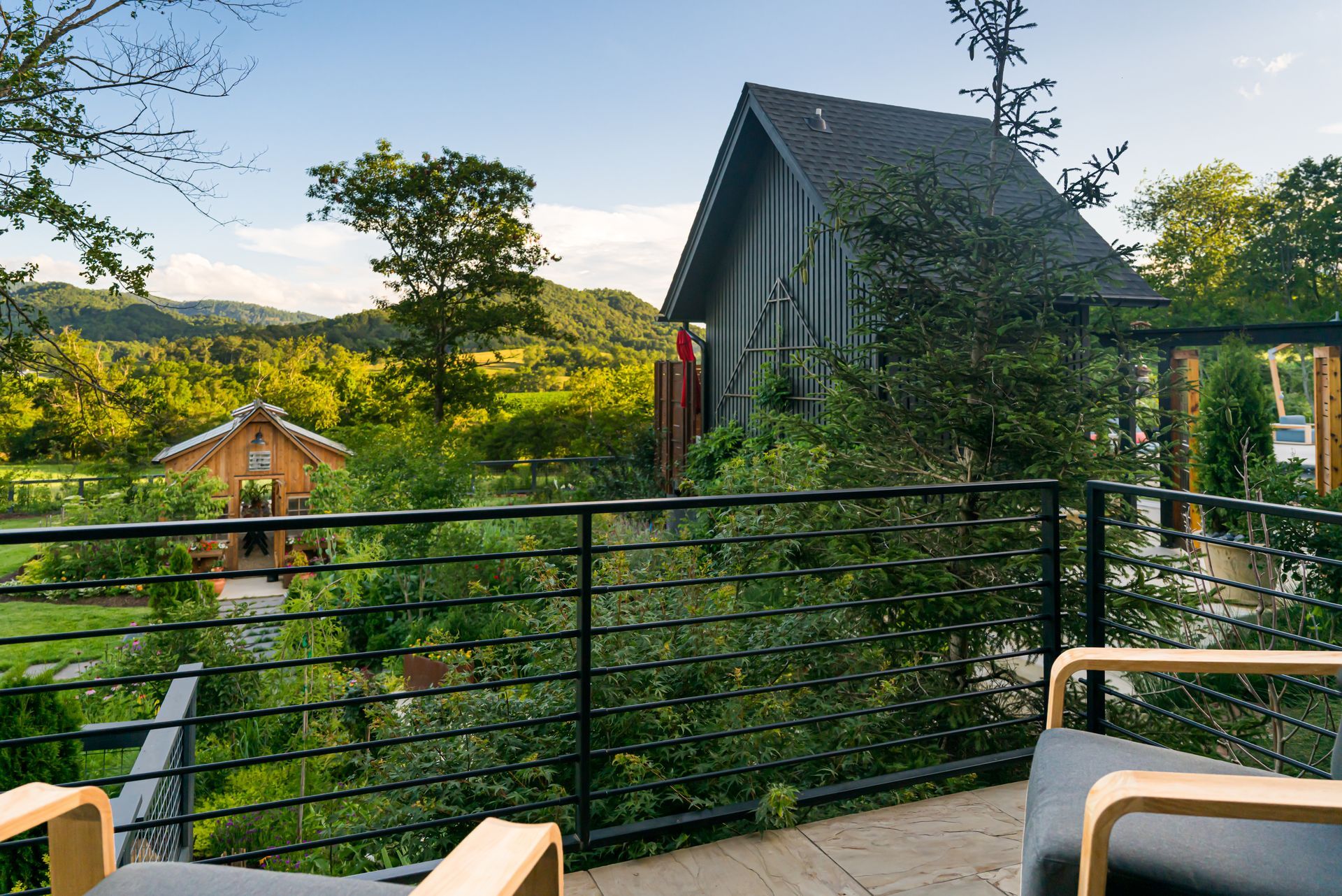 Deck with chairs overlooking a lush hillside and a dark-roofed cabin at sunset