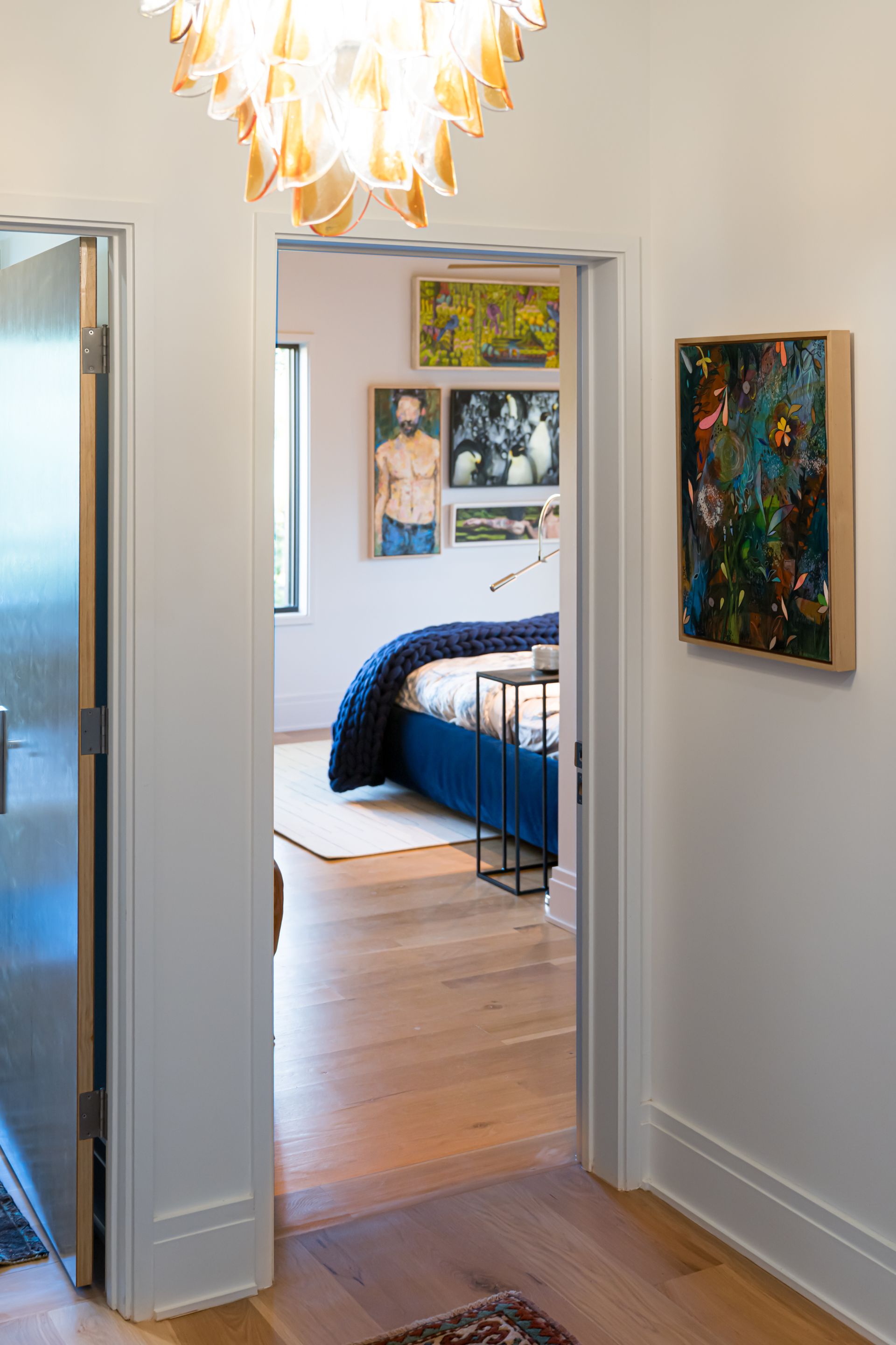 Hallway view into a bedroom with blue bedding, framed art, and wood floors