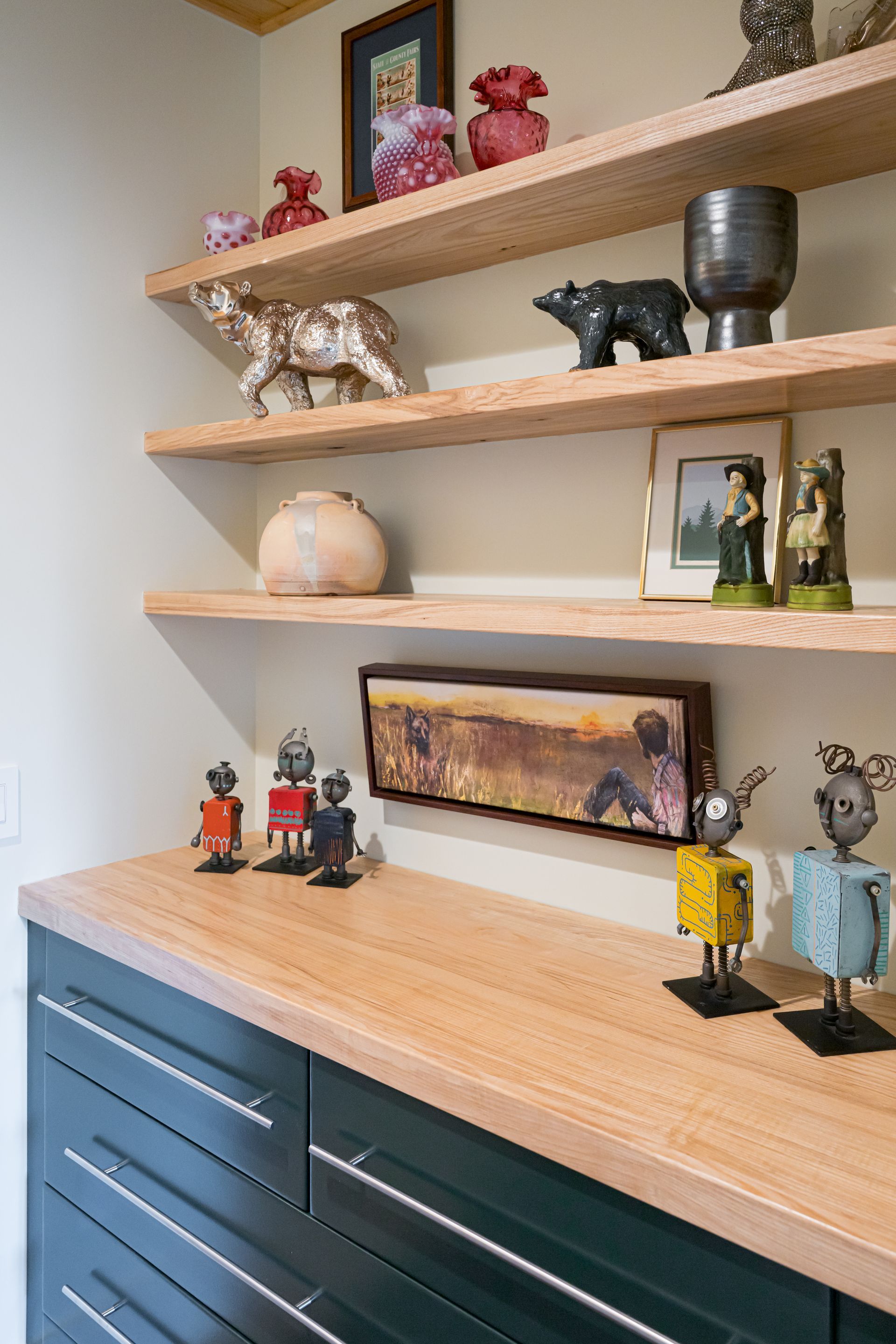 Wood shelves above a blue cabinet display small sculptures, framed art, and decor in a modern room
