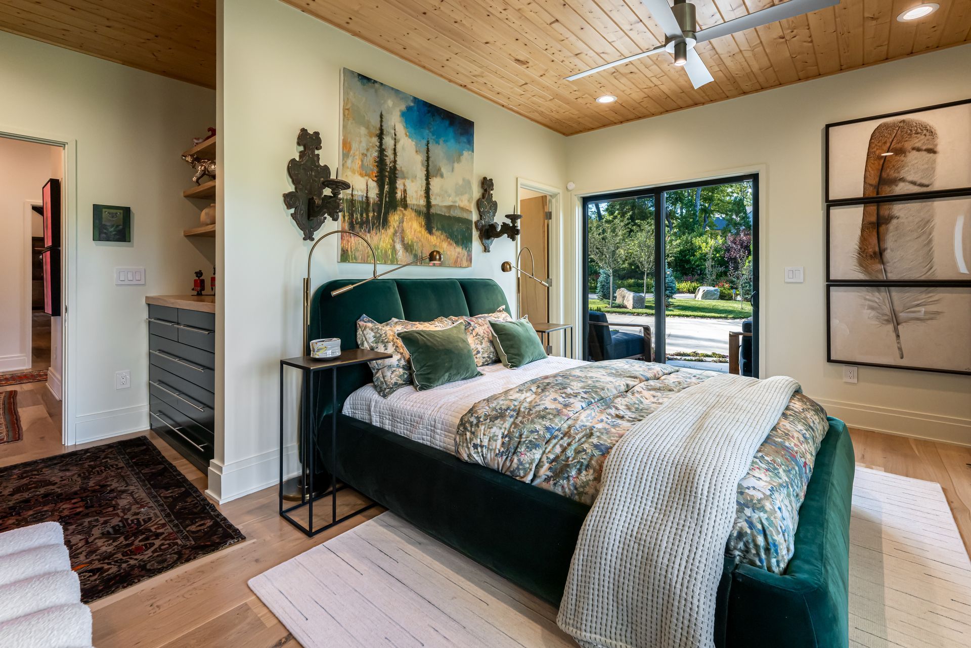 Bright bedroom with teal bed, abstract wall art, and large windows overlooking greenery