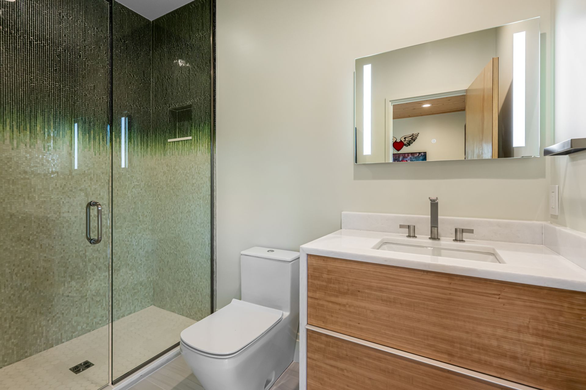 Modern bathroom with glass shower, toilet, and wood vanity with mirror.
