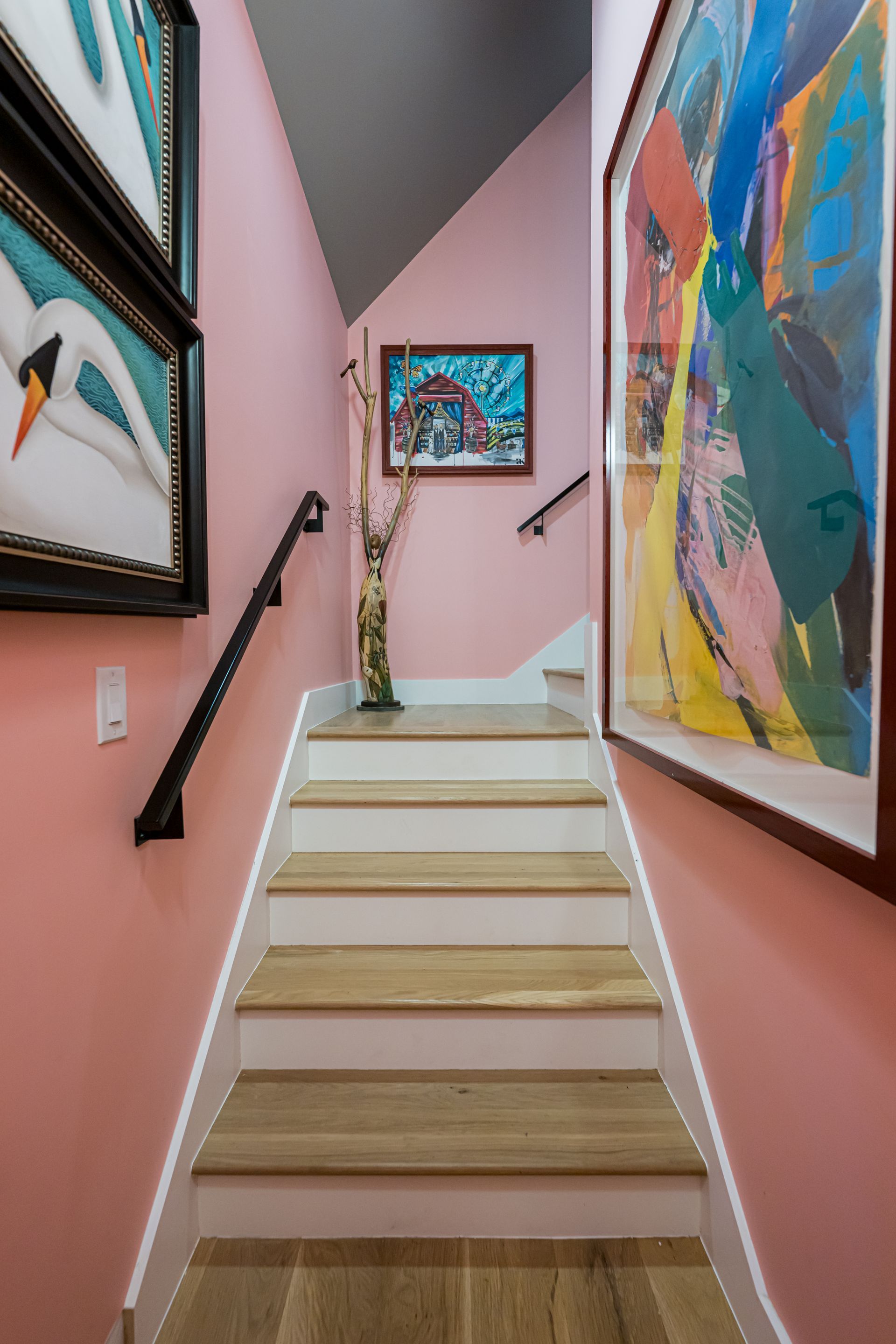 Narrow pink staircase with framed colorful abstract art on both walls and a small plant at the landing