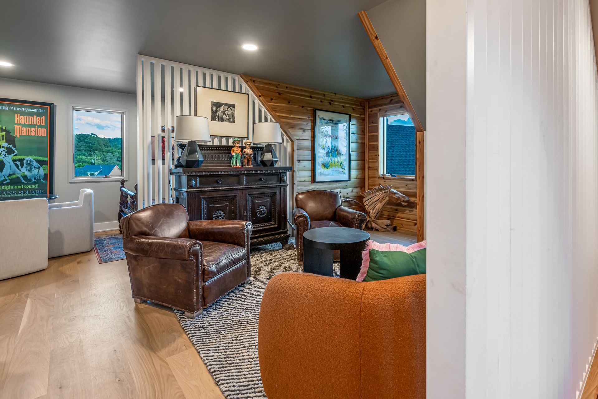 Cozy living room with leather chairs, fireplace, patterned rug, and large windows in warm lighting