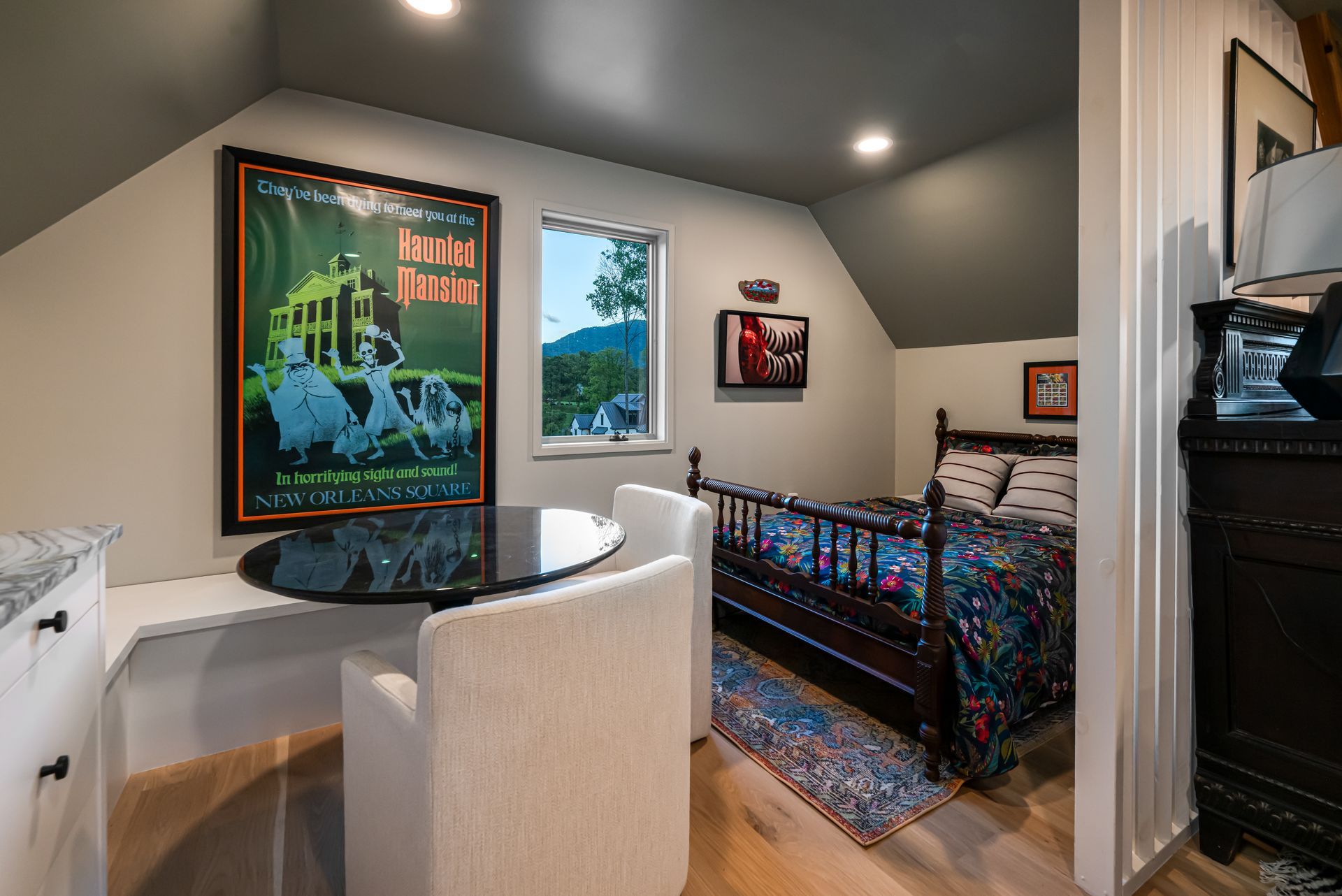 Small bedroom with a bed, desk chair, framed poster, and window overlooking trees.