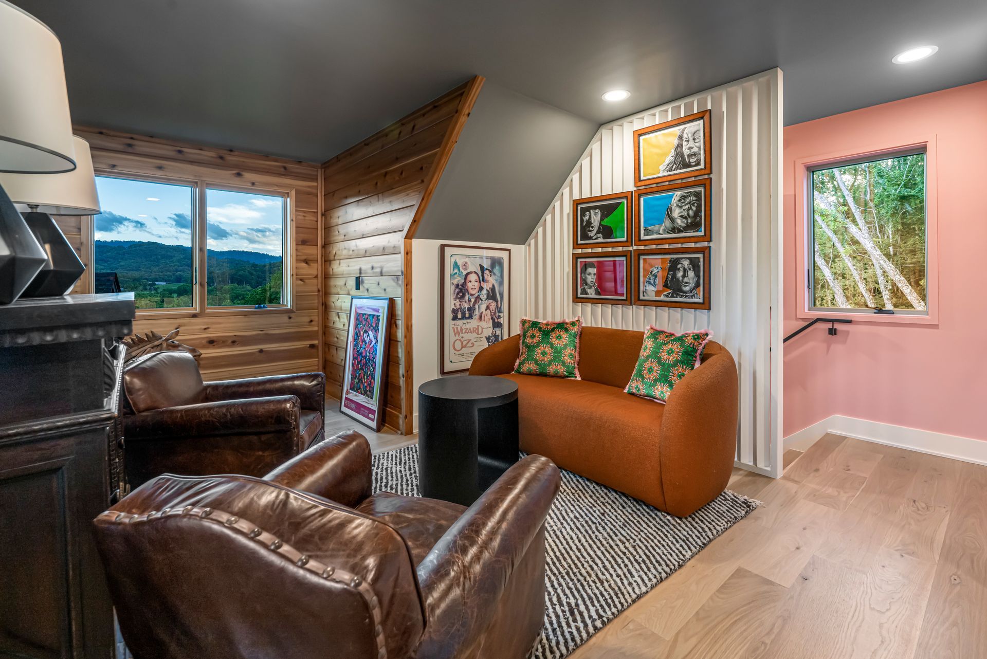 Cozy attic living room with brown leather chairs, orange sofa, pink walls, and large windows overlooking mountains