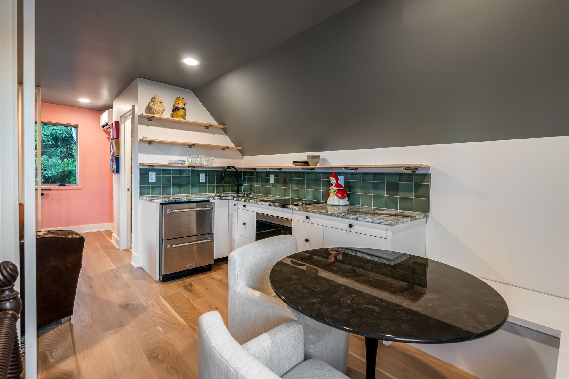 Modern kitchen with stainless appliances, teal tile backsplash, and round black table with white chairs.