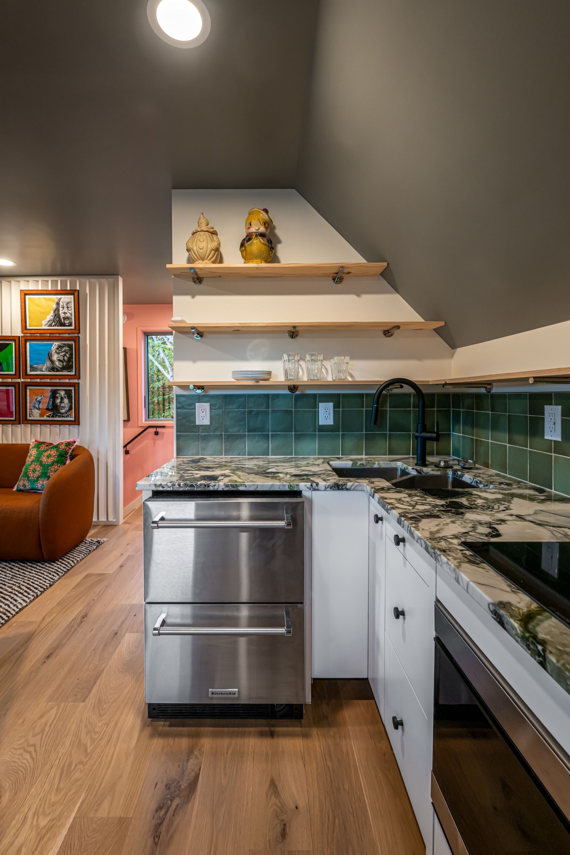 Modern kitchen with stainless dishwasher, green tile backsplash, granite counters, and wood flooring