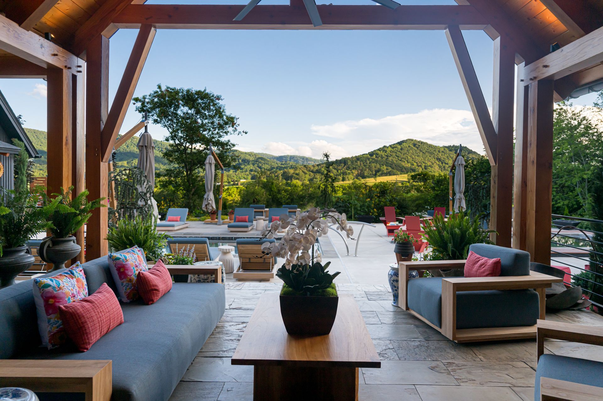 Covered patio with lounge seating, pool, and mountain view beyond a garden