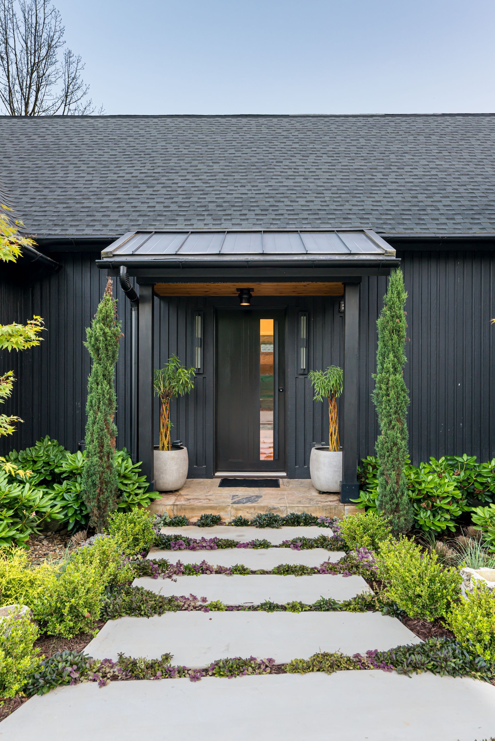 Modern black house entrance with stone walkway and landscaped greenery