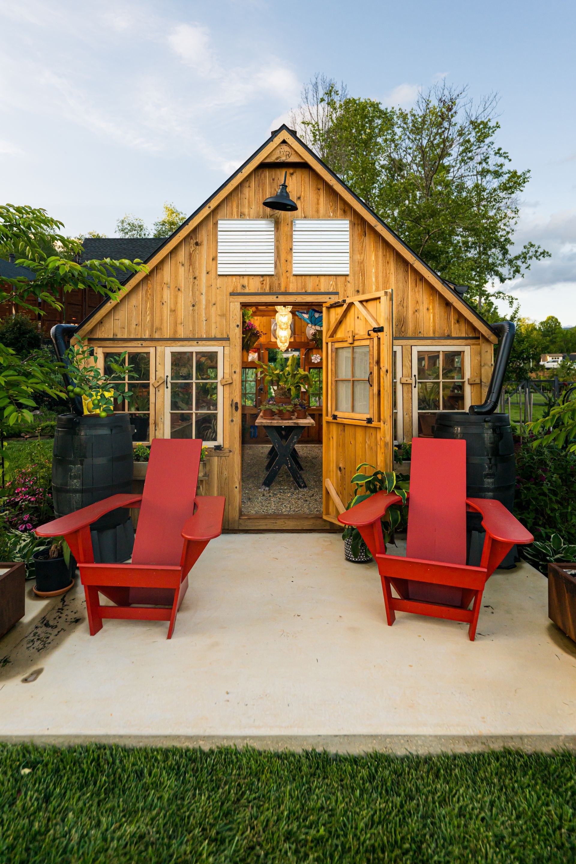 Rustic garden greenhouse with open wooden doors and two red chairs on a patio.
