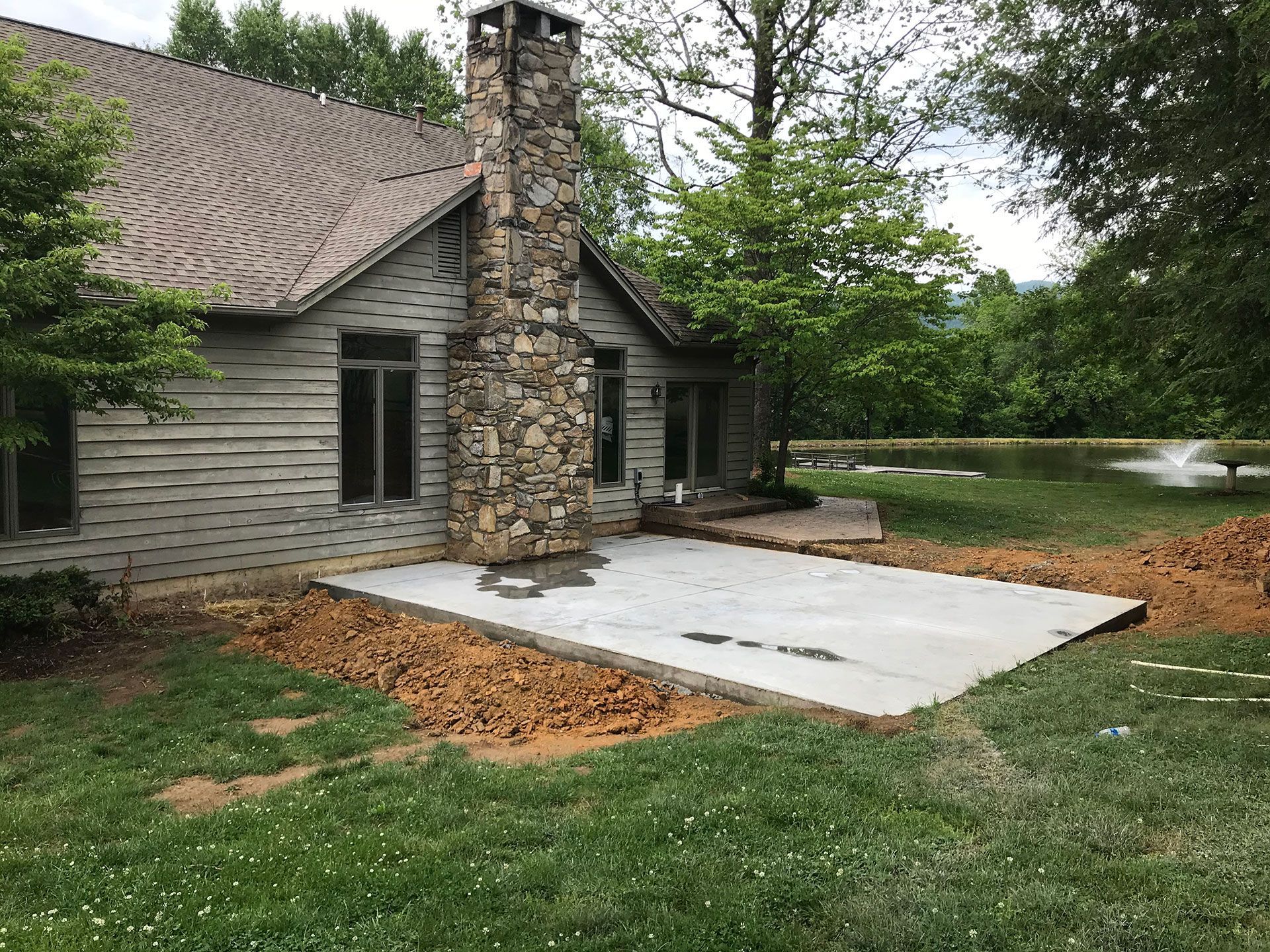 A house with a stone chimney and a concrete patio in front of it.