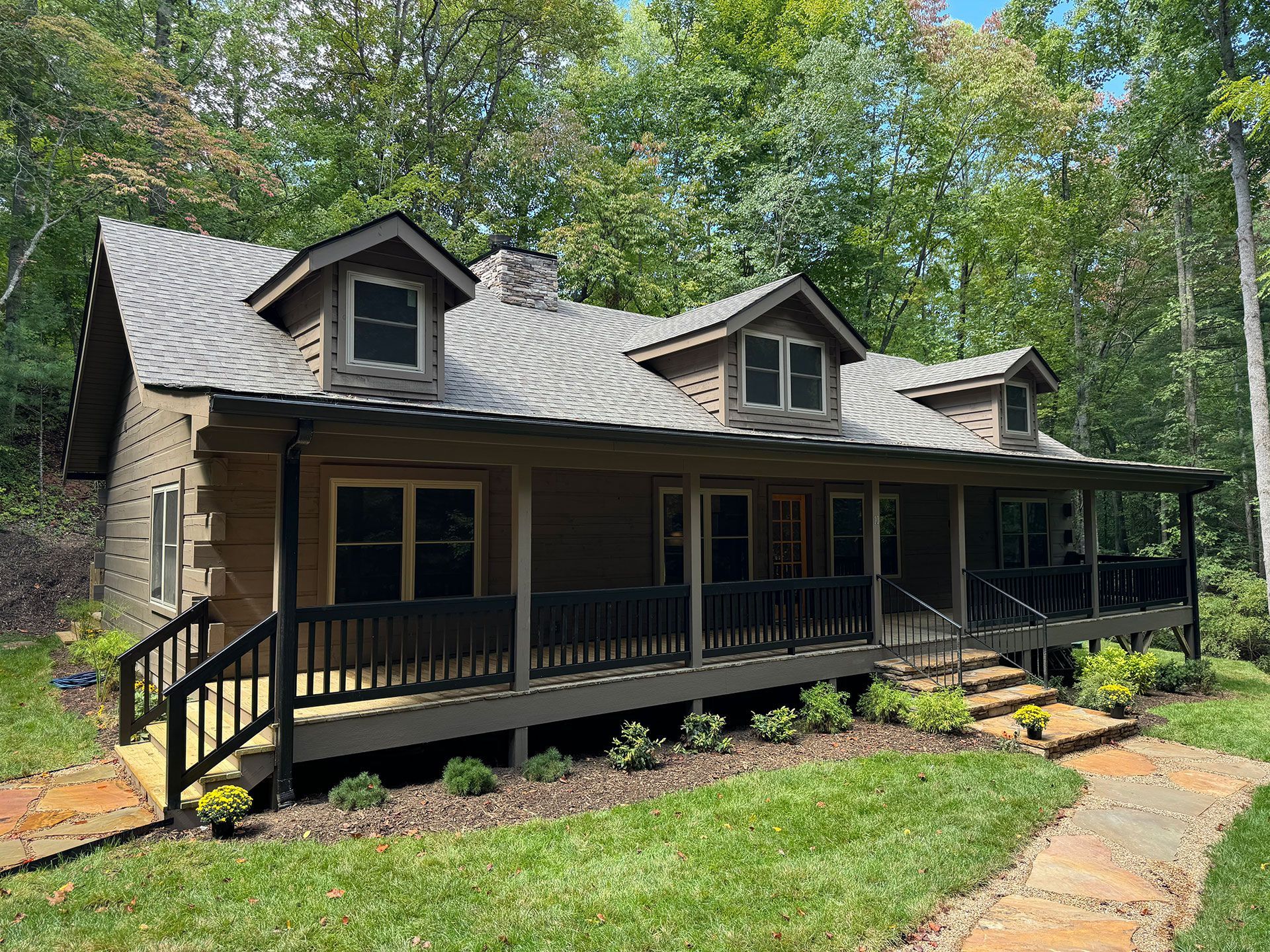 A large house with a large porch in the middle of the woods.