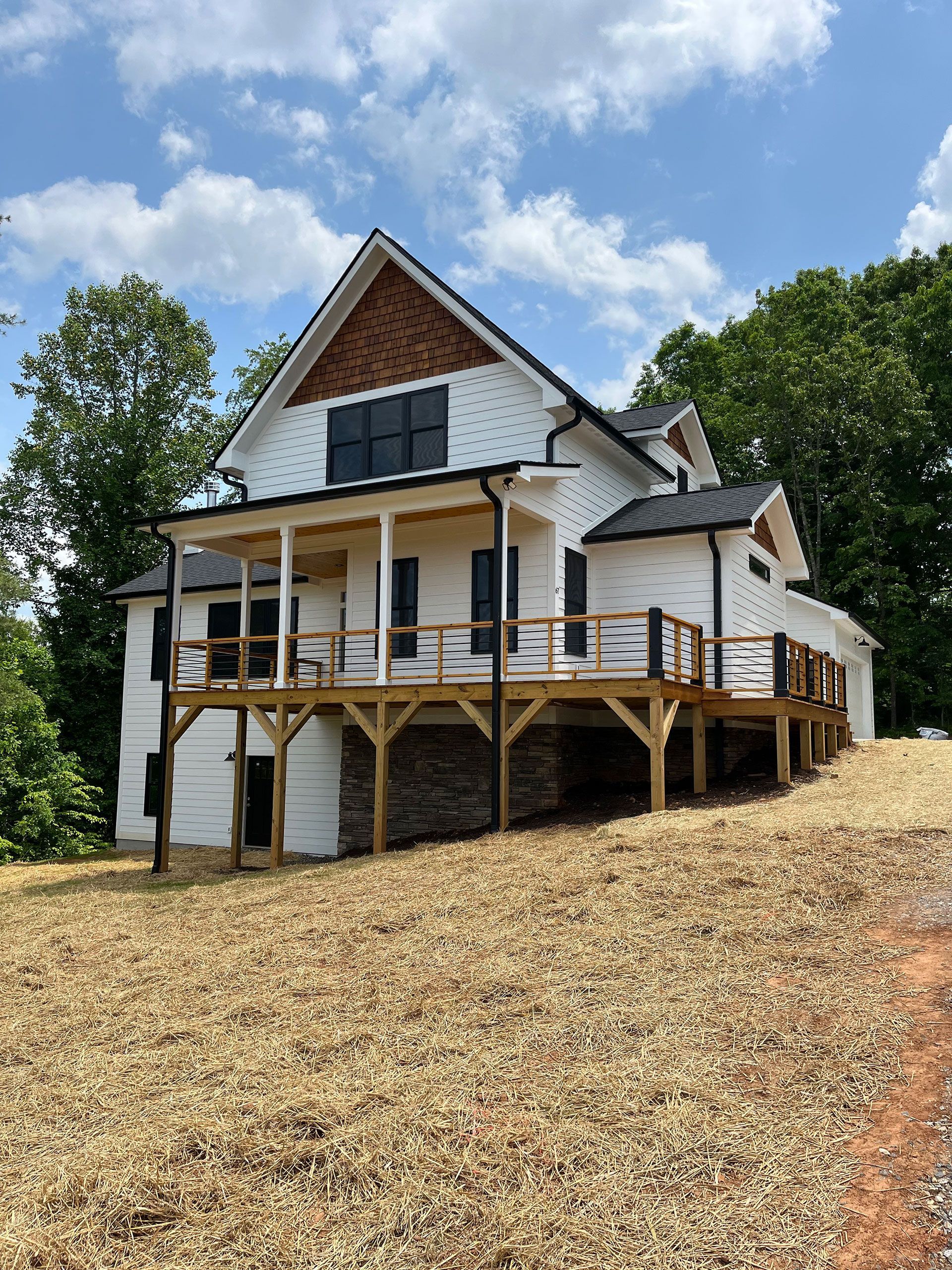 A white house with a large deck is sitting on top of a hill.