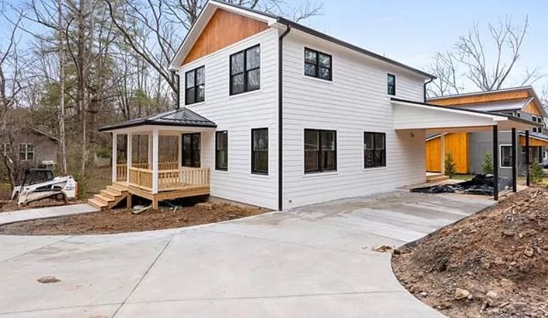 A white house with a porch and a concrete driveway in front of it.