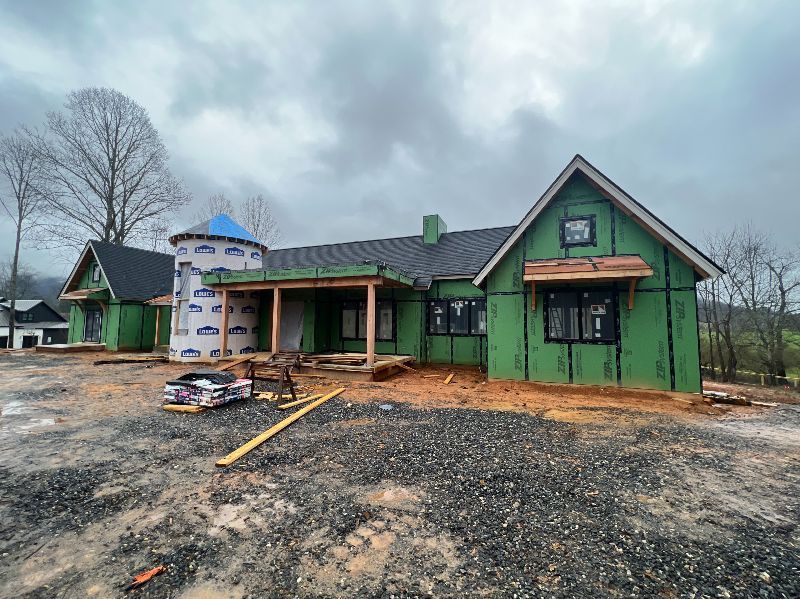 A house is being built with green siding and a silo in the background.