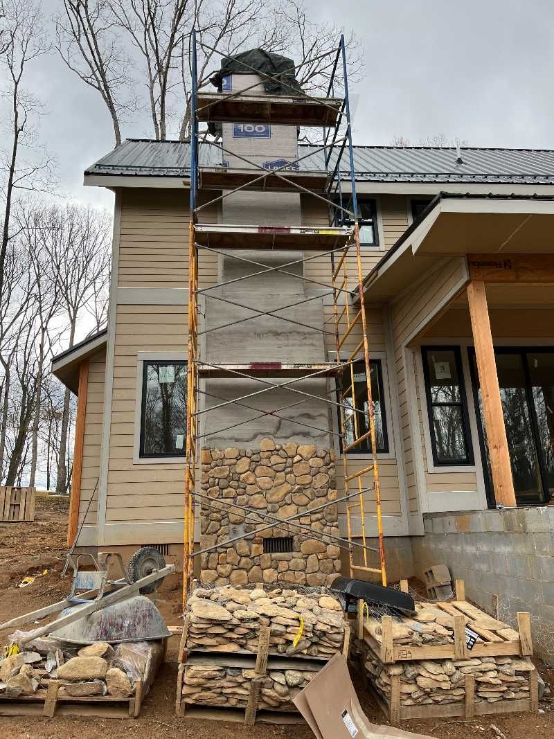 A large stone fireplace is being built on the side of a house.