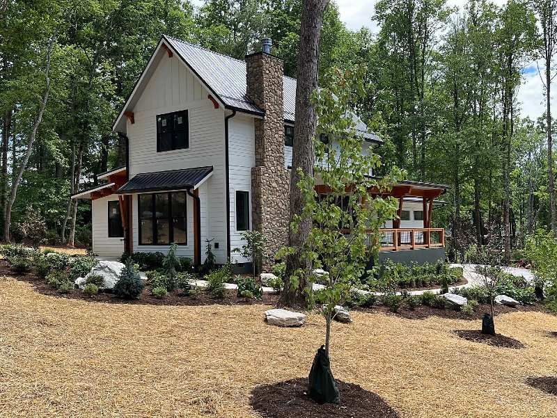 A white house with a stone chimney is surrounded by trees.