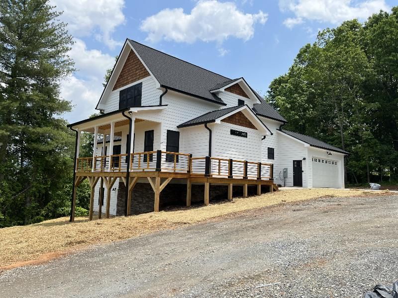 A large white house with a large deck is sitting on top of a hill.