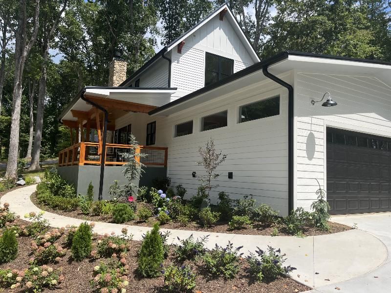 A white house with a black garage door is surrounded by trees